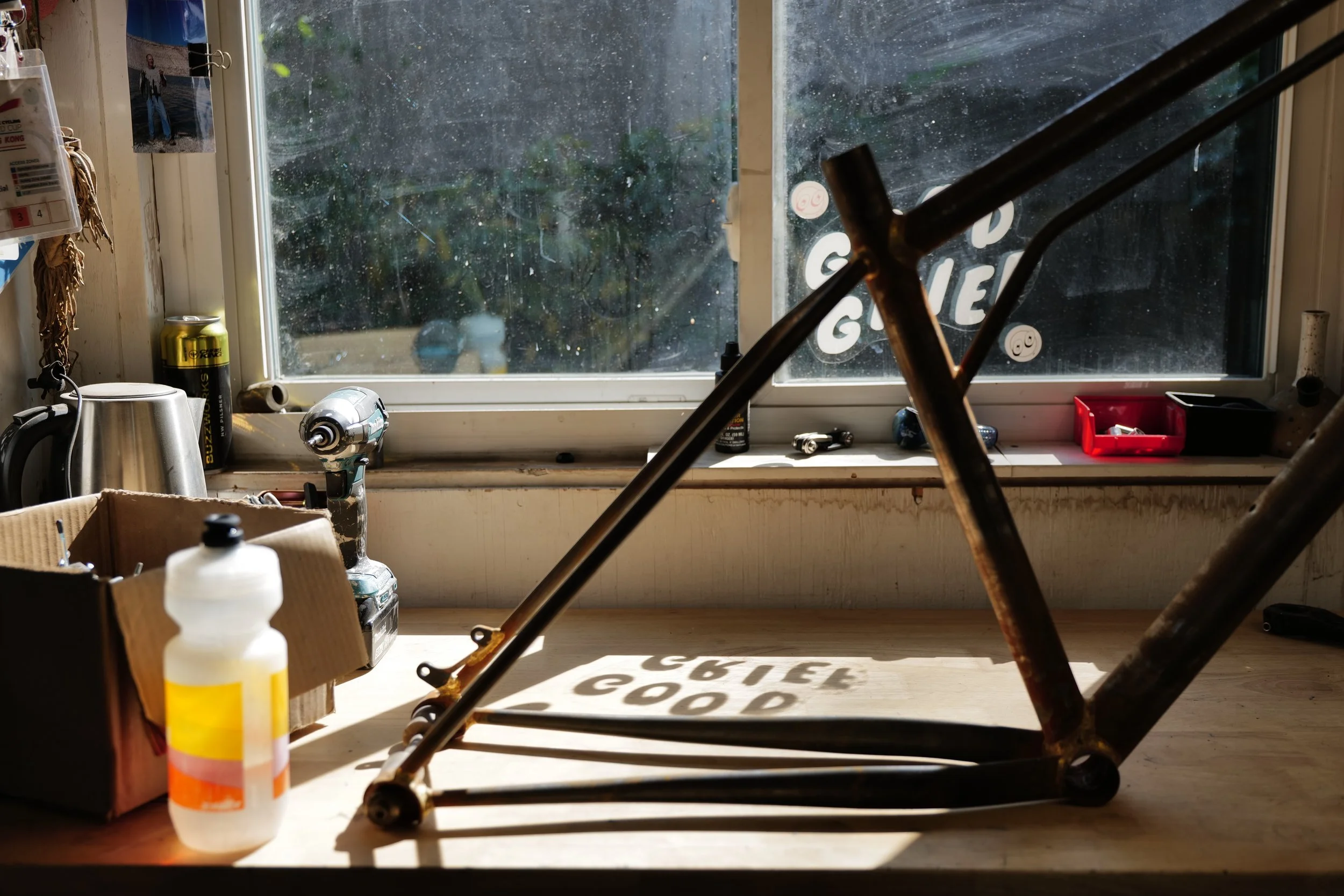  A bicycle frame sat on a workbench in front of a window with the sun streaming through 