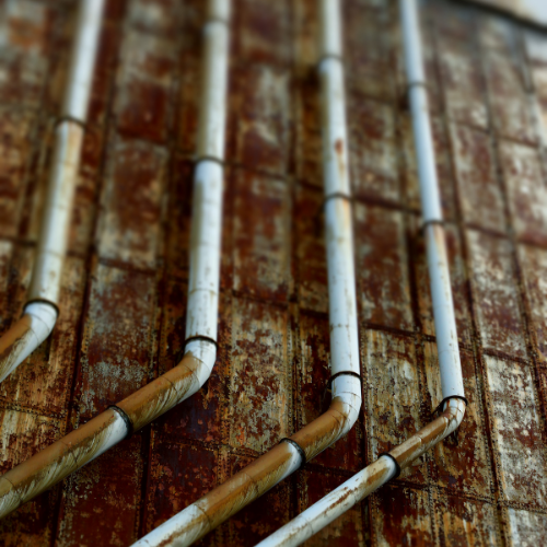 Multiple white pipes attached to a rusted metal wall. Norwich Plumbing and Heating Ltd.