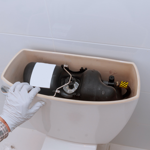 A person wearing a white glove holding a disassembled toilet fill valve inside a toilet tank. Norwich Plumbing and Heating Ltd.