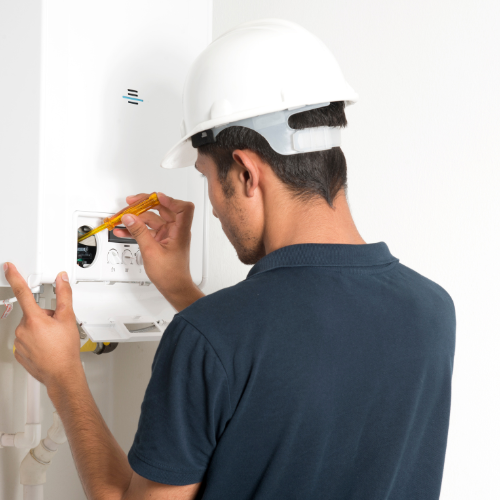A technician wearing a white hard hat and navy shirt working on a gas meter with a screwdriver. Norwich Plumbing and Heating Ltd.