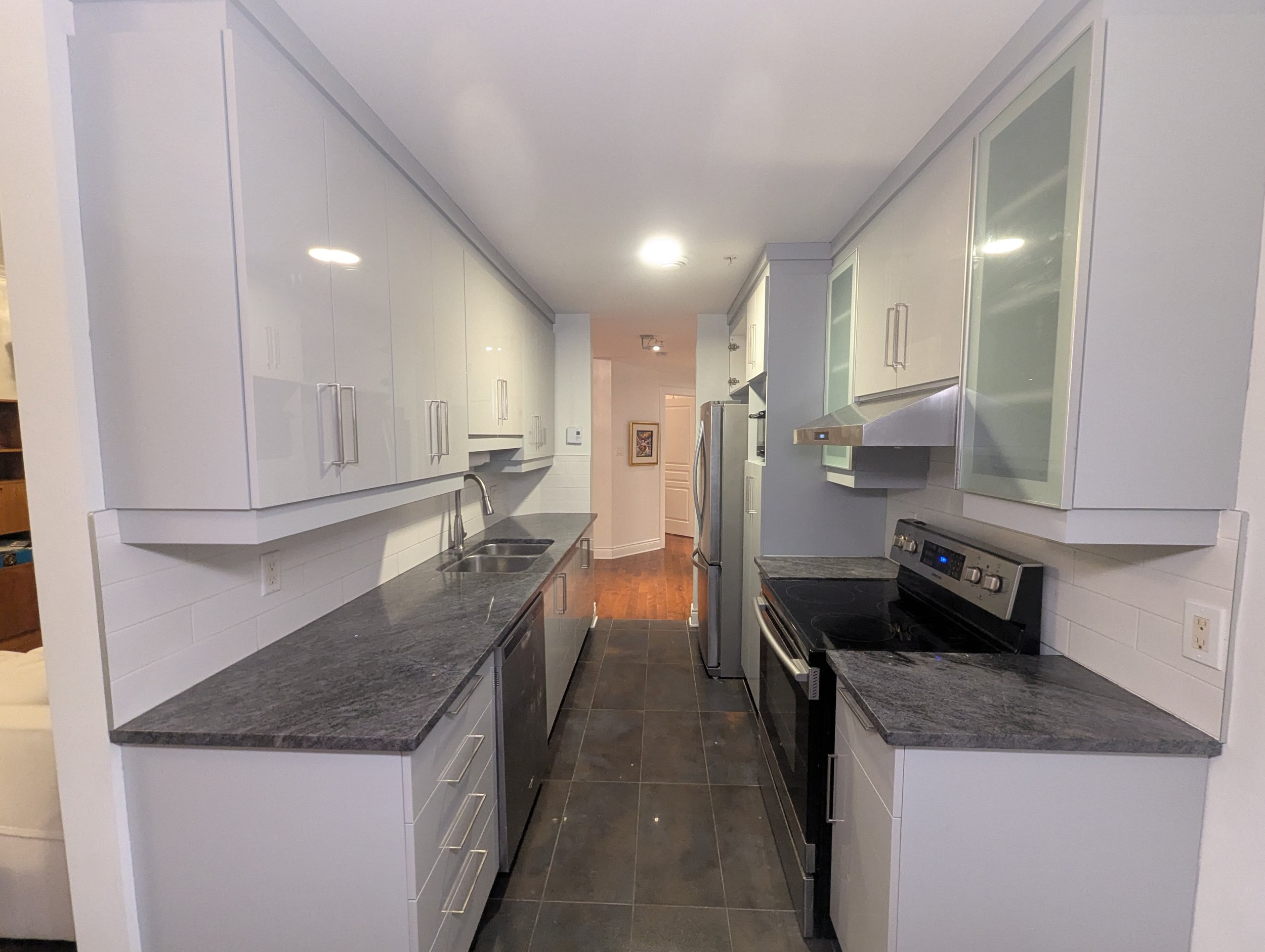 Modern kitchen with white cabinets, dark granite countertops, stainless steel appliances, and black tile flooring.