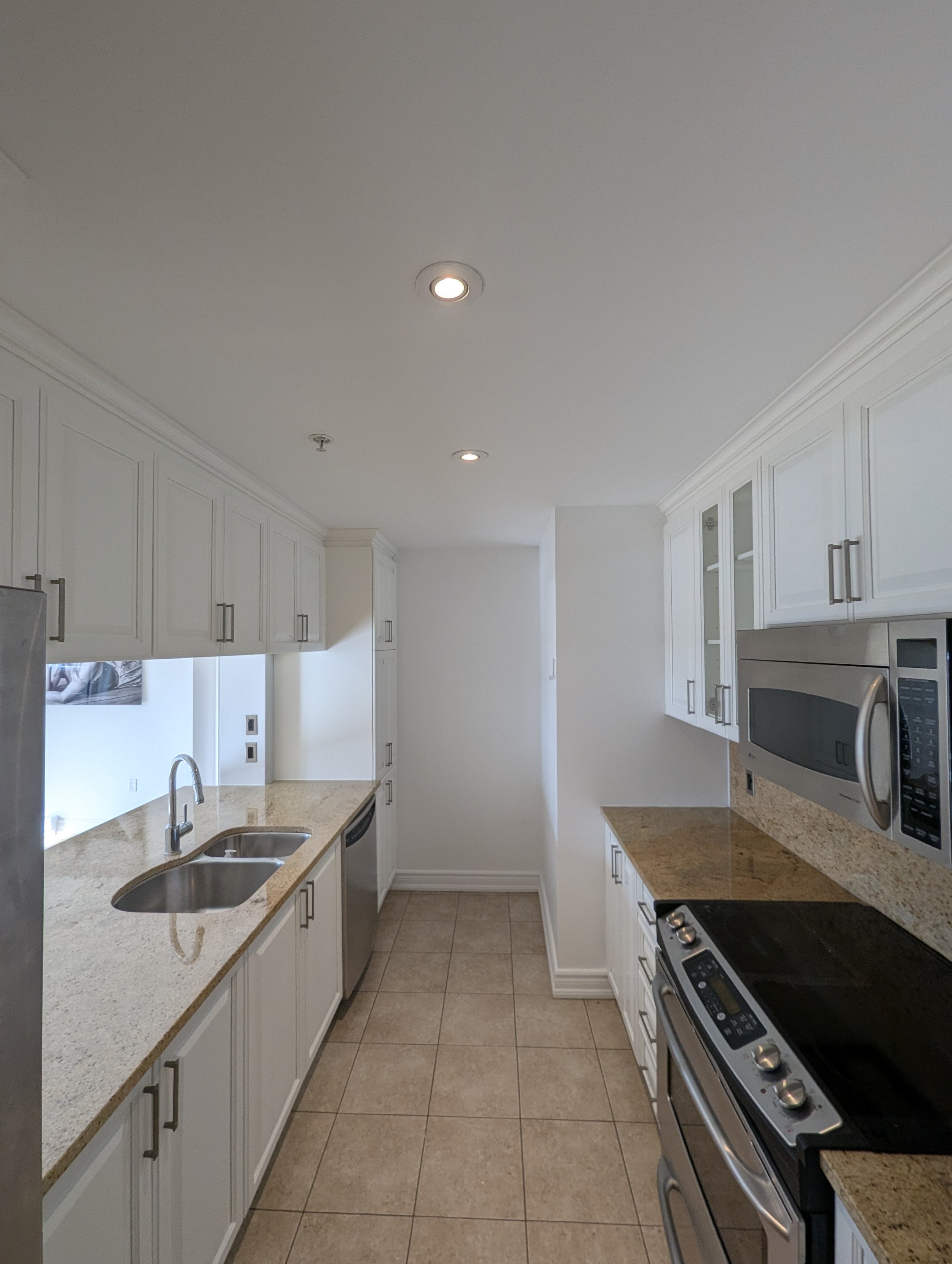 A modern kitchen with white cabinets, granite countertops, stainless steel appliances including a microwave and oven, and beige tiled flooring.