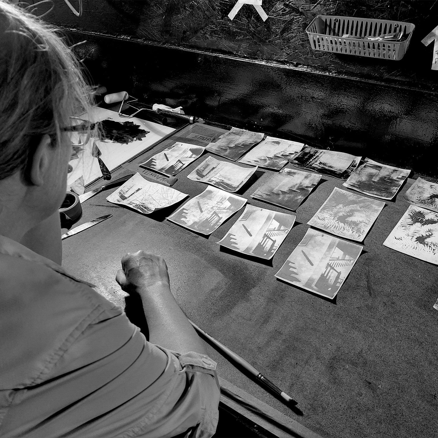 Colleen Graham studying small bromoil photographs on darkroom table.
