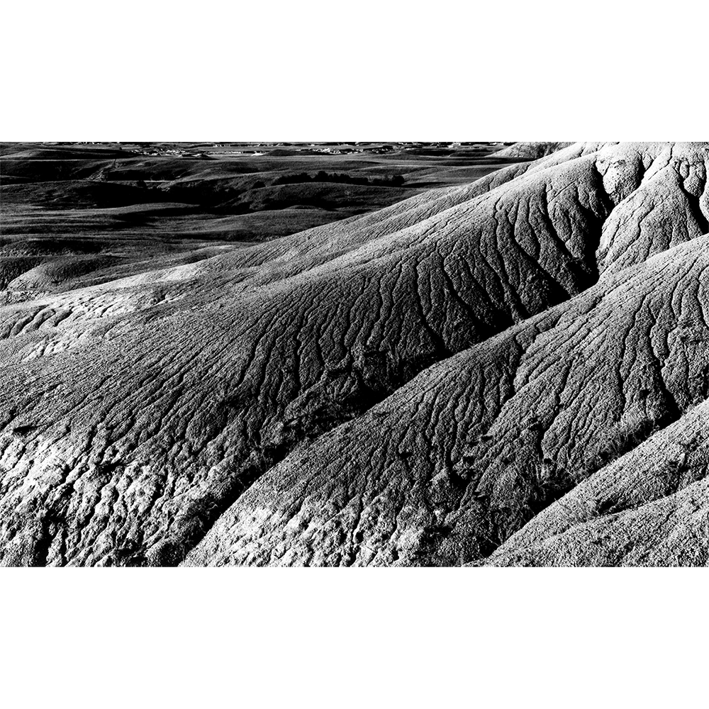 Silver gelatin photograph 'Dirt' — eroded badlands ridges and furrowed earth above distant rolling plains, hand-printed.