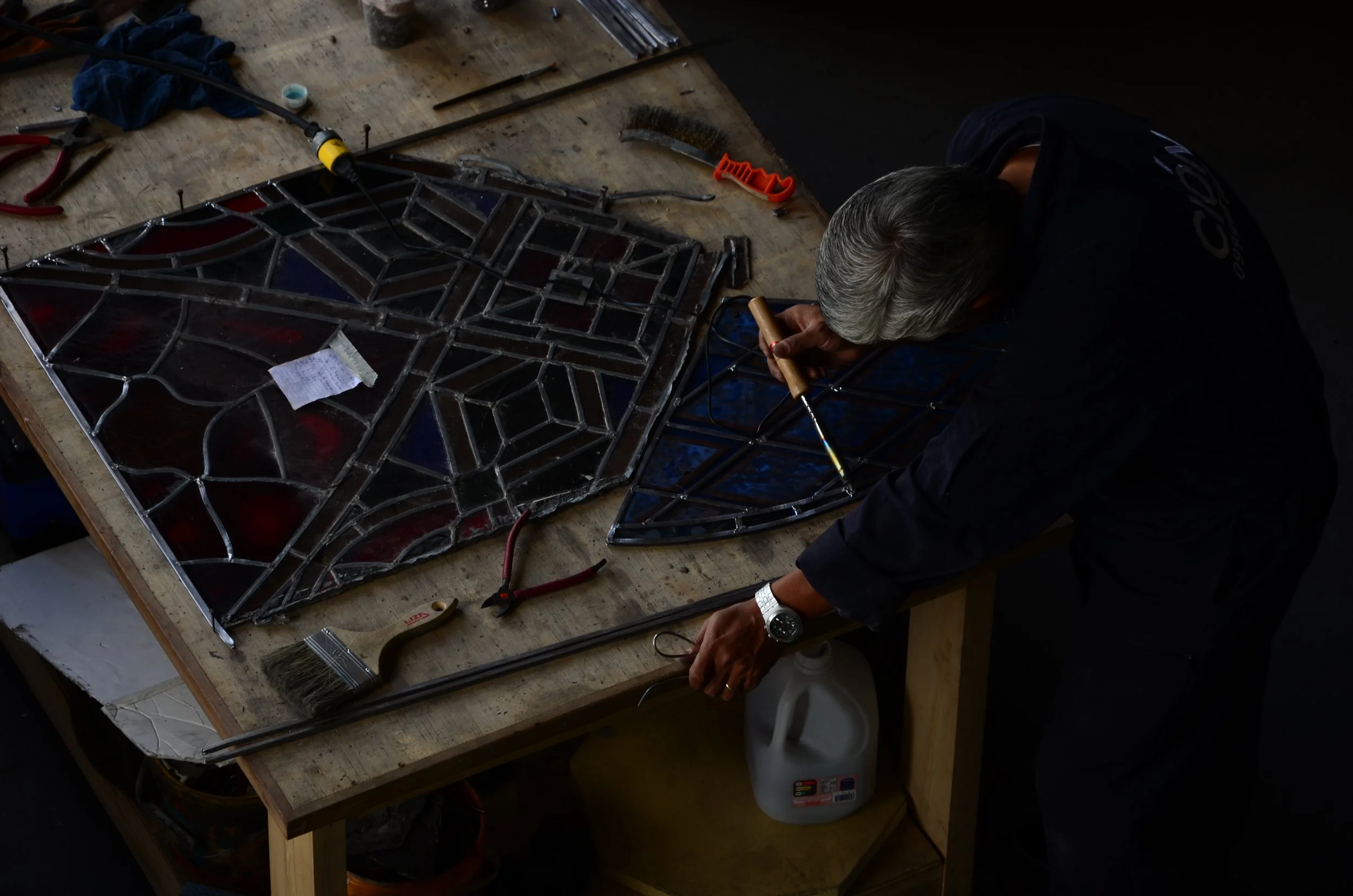 A person working on restoring or assembling stained glass windows at a workbench surrounded by tools.