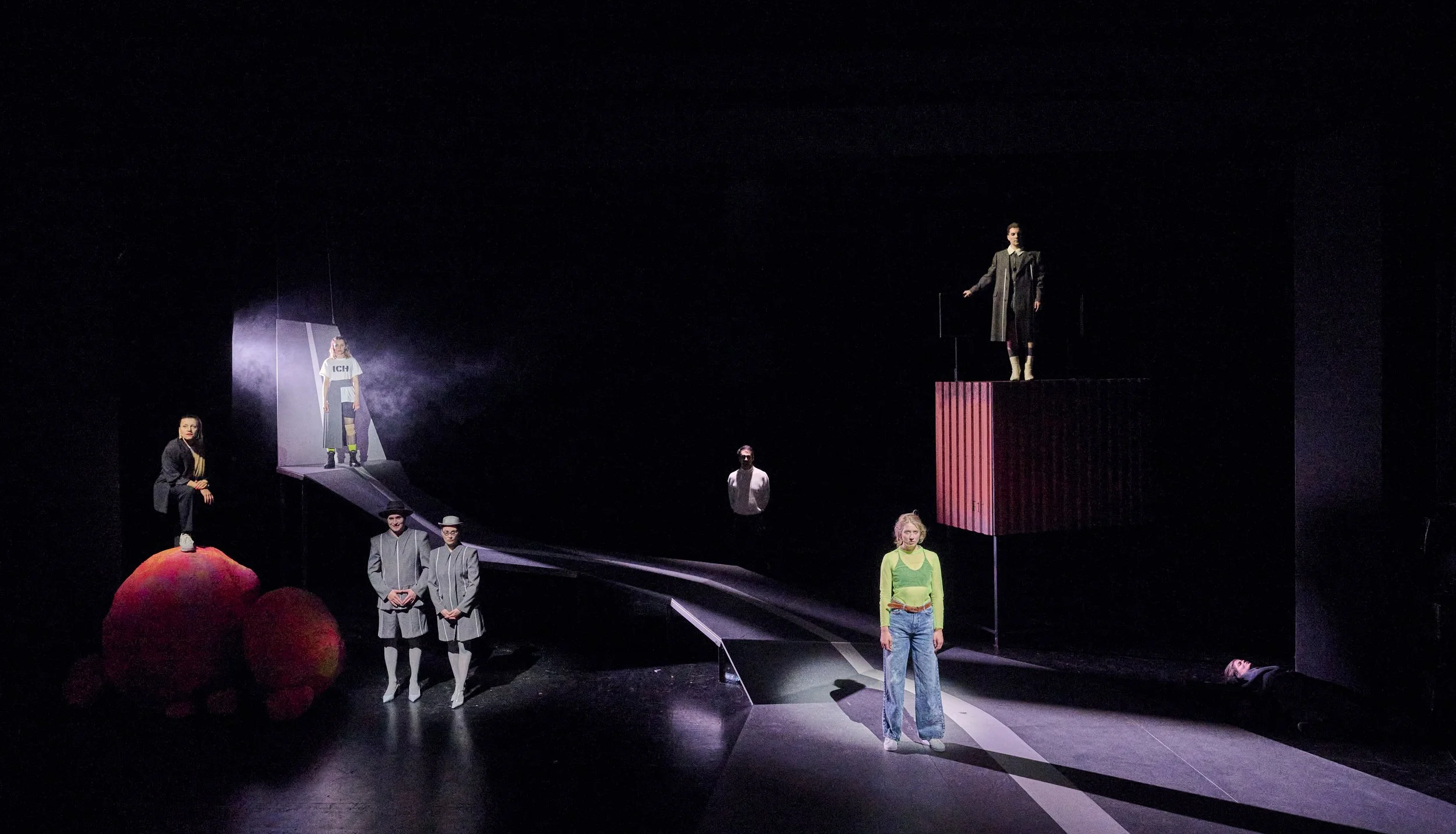 Theaterbühne mit mehreren Schauspielern in unterschiedlichen Szenen, dunkler Hintergrund, spezielle Beleuchtung, moderne Kostüme.