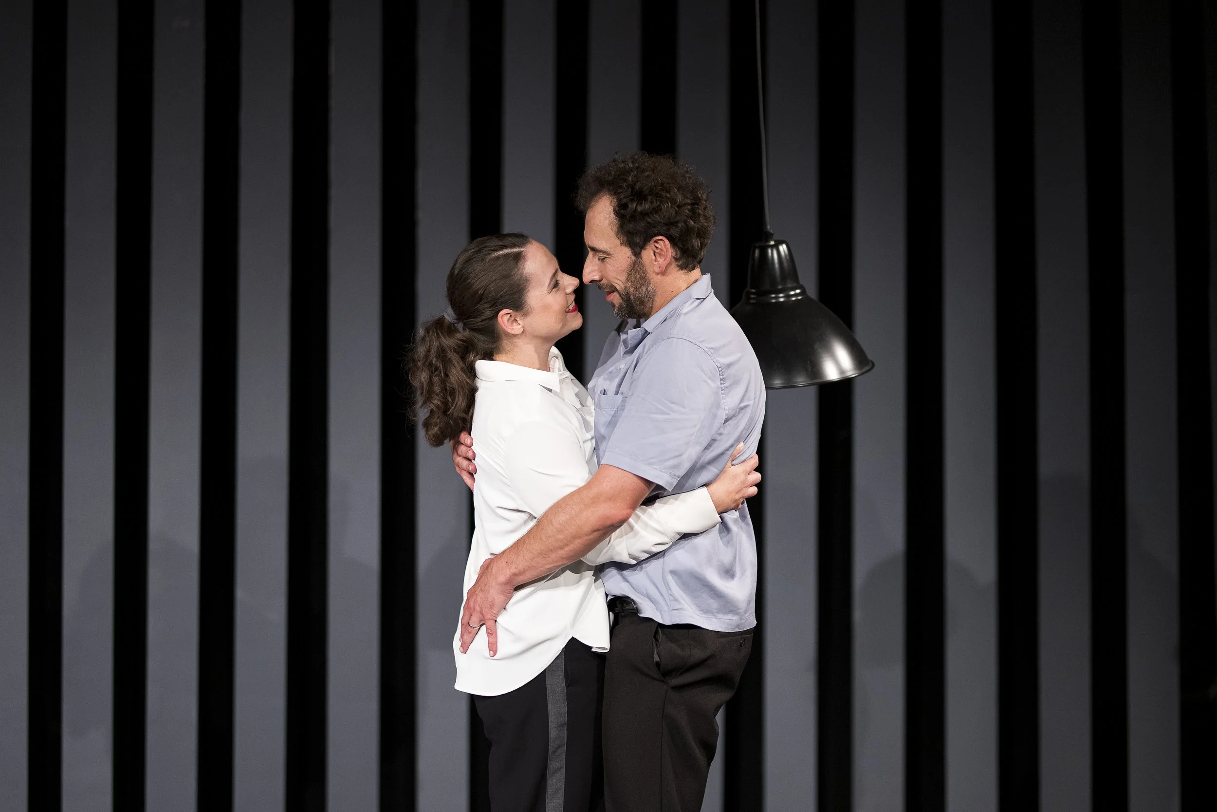 Zwei Menschen umarmen sich und blicken sich in die Augen auf einer Bühnenausschnitt.