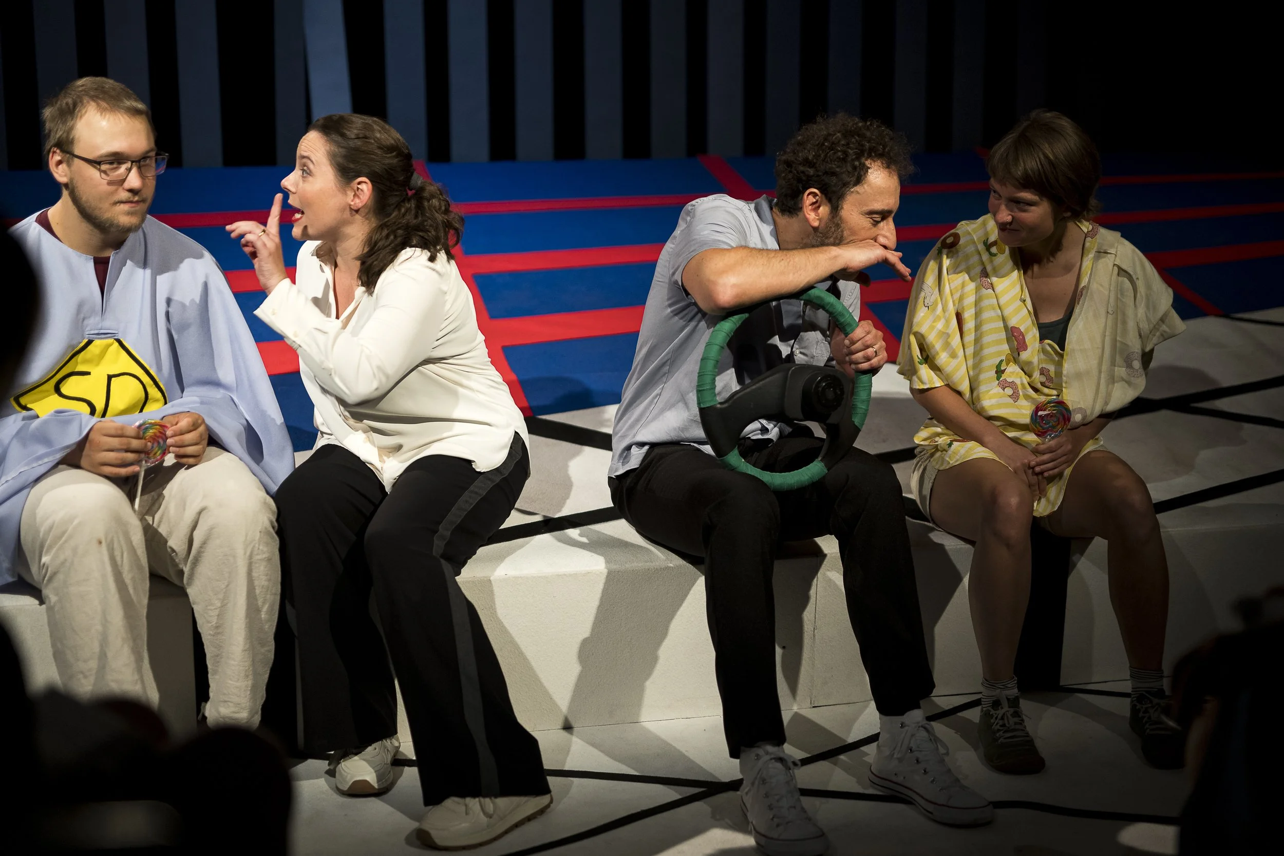 Menschen auf einer Bühne bei einer Theateraufführung, im Hintergrund eine schwarze Kulisse.