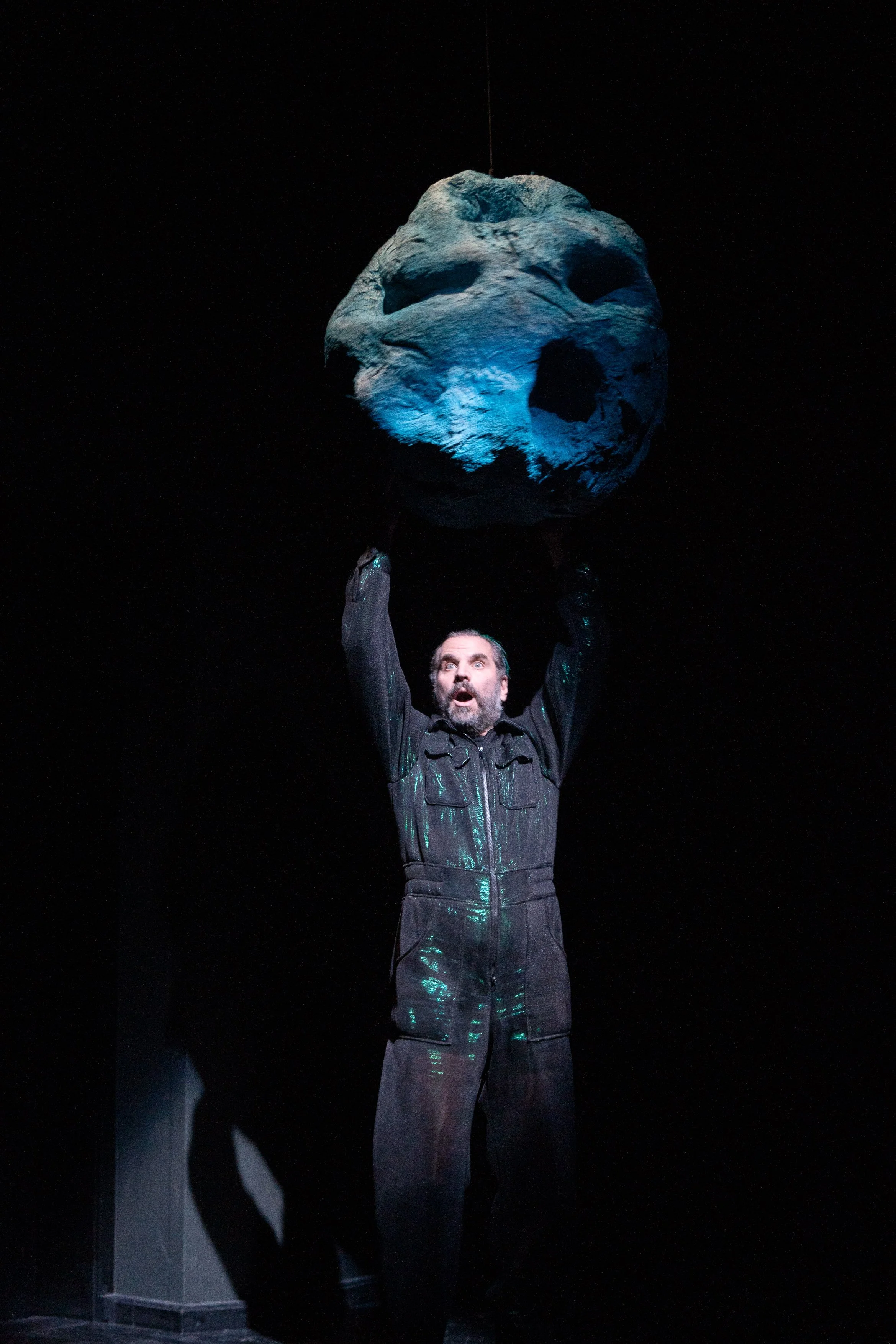 Mann in dunkler Kleidung hält einen leuchtenden, mit Löchern versehenen Ball in der Hand in dunklem Raum.