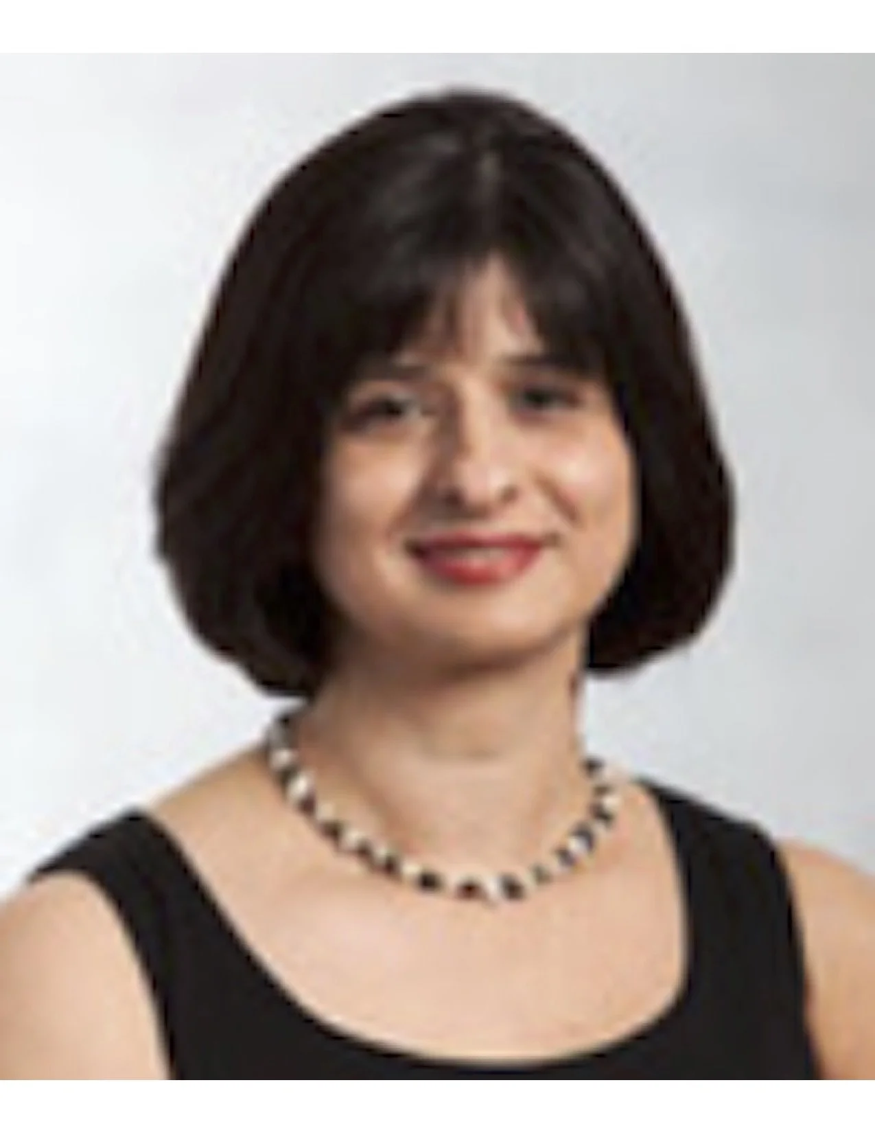 Portrait of a woman with short dark hair, wearing a black sleeveless top, a black and white beaded necklace, and red lipstick, smiling at the camera.