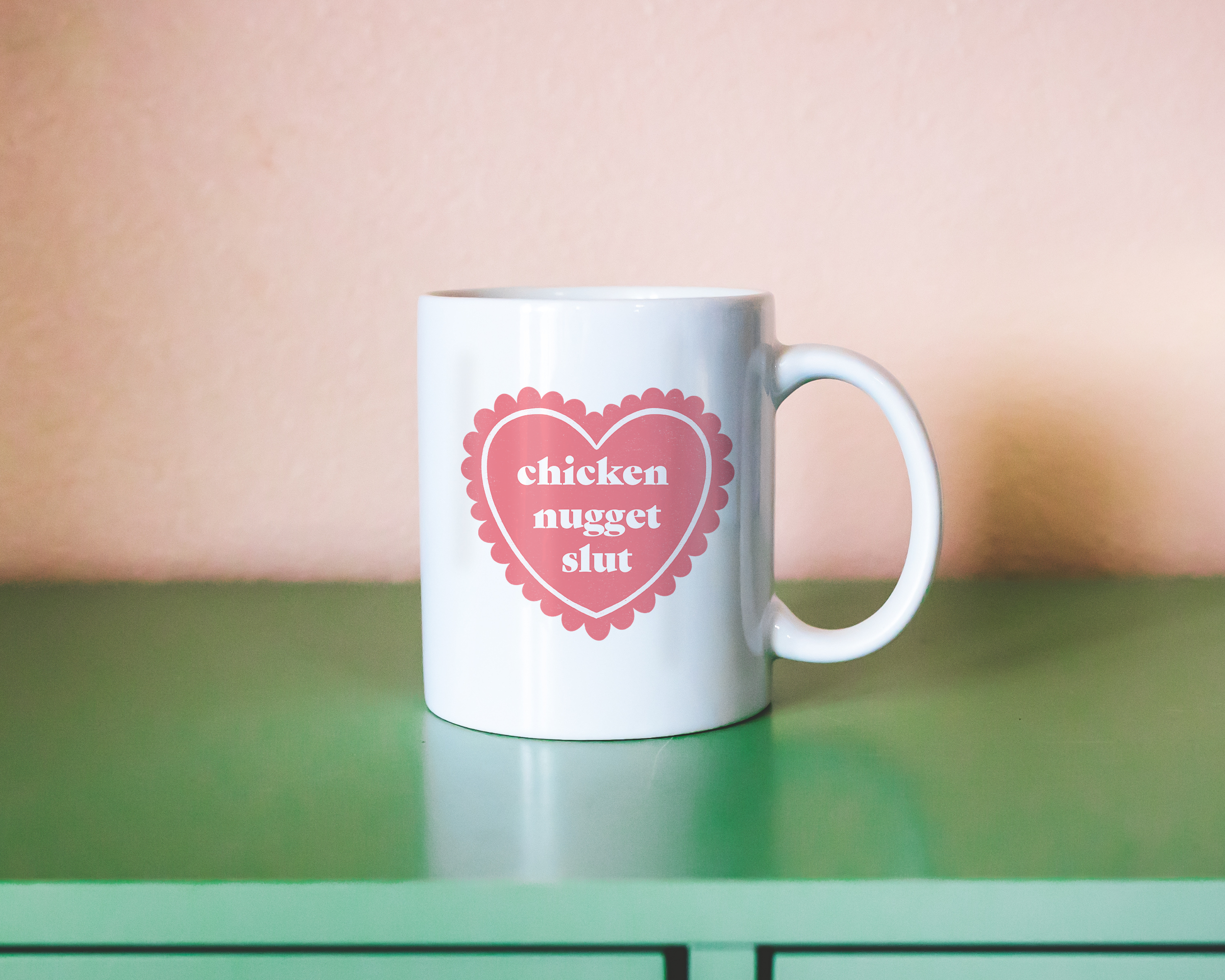 Sassy dopamine decor White coffee mug that says "chicken nugget slut" in a retro vintage style frilly heart that's pink with a retro font.. Available in 11oz and 15oz