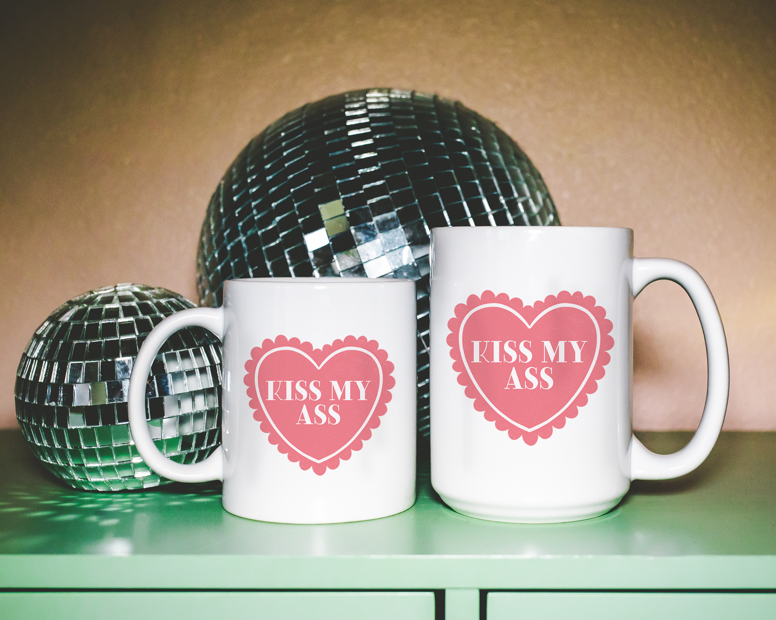 Sassy dopamine decor White coffee mug that says "kiss my ass" in a retro vintage style frilly heart that's pink with a retro font.. Available in 11oz and 15oz