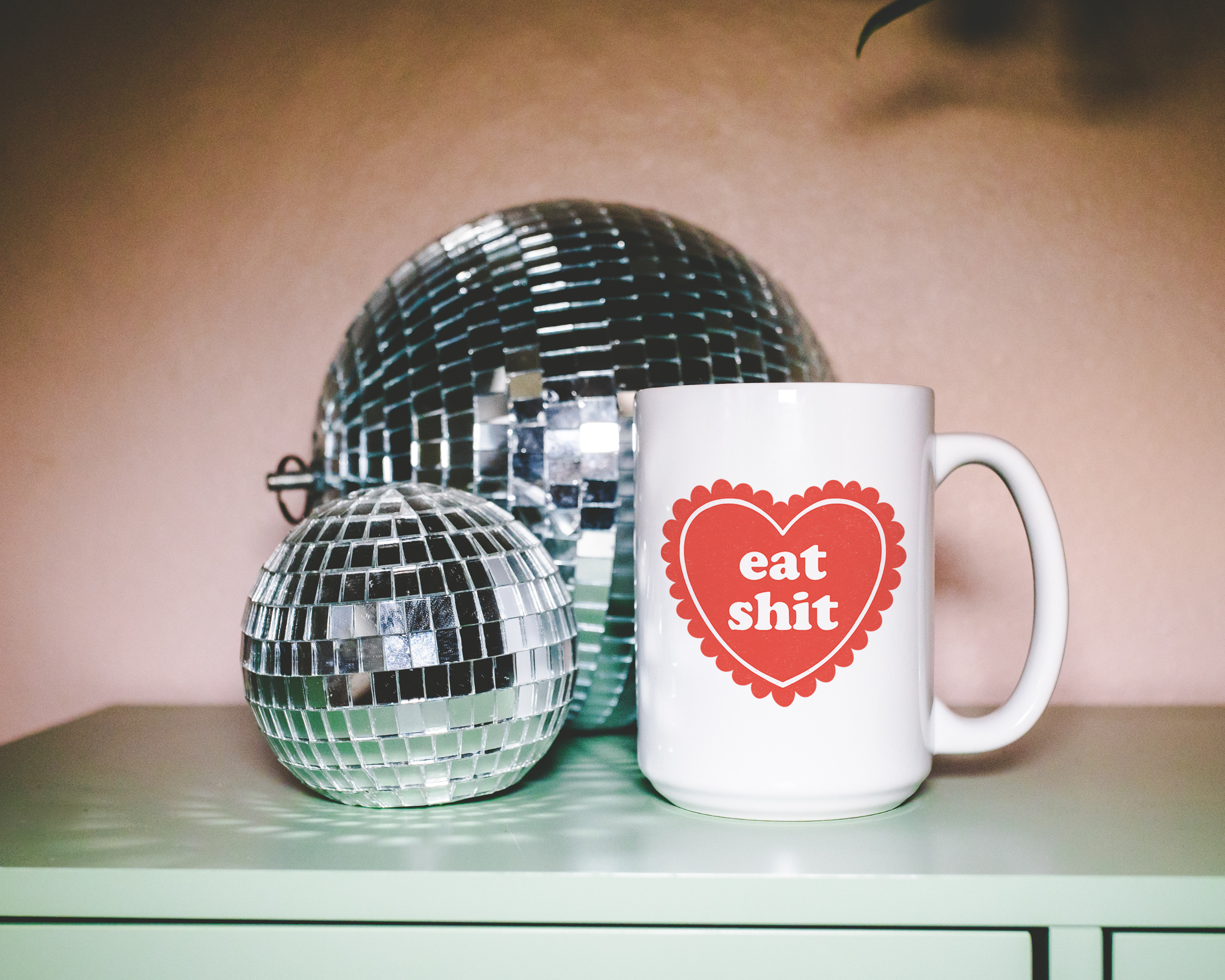 Sassy dopamine decor White coffee mug that says "Eat shit" in a retro vintage style frilly heart that's red with a retro font.. Available in 11oz and 15oz