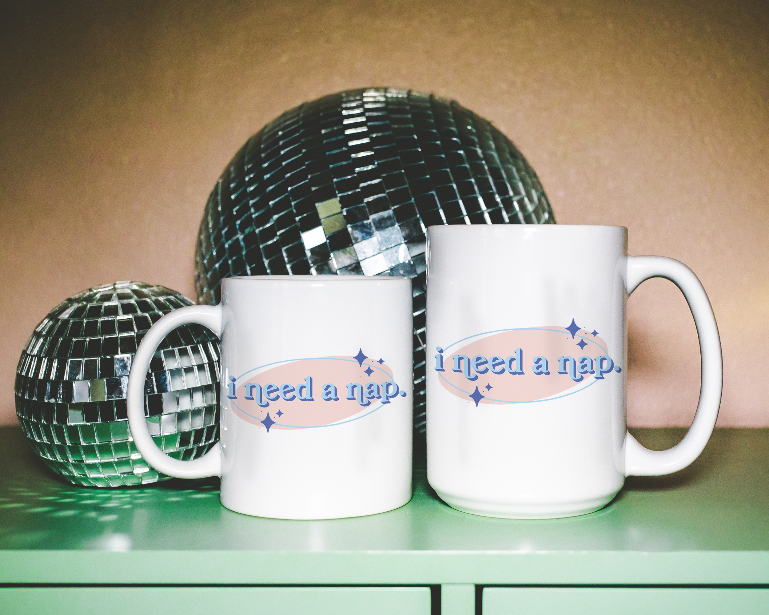 White coffee mug that says "I need a nap" in a retro vintage font that's blue and pink. Available in 11oz and 15oz