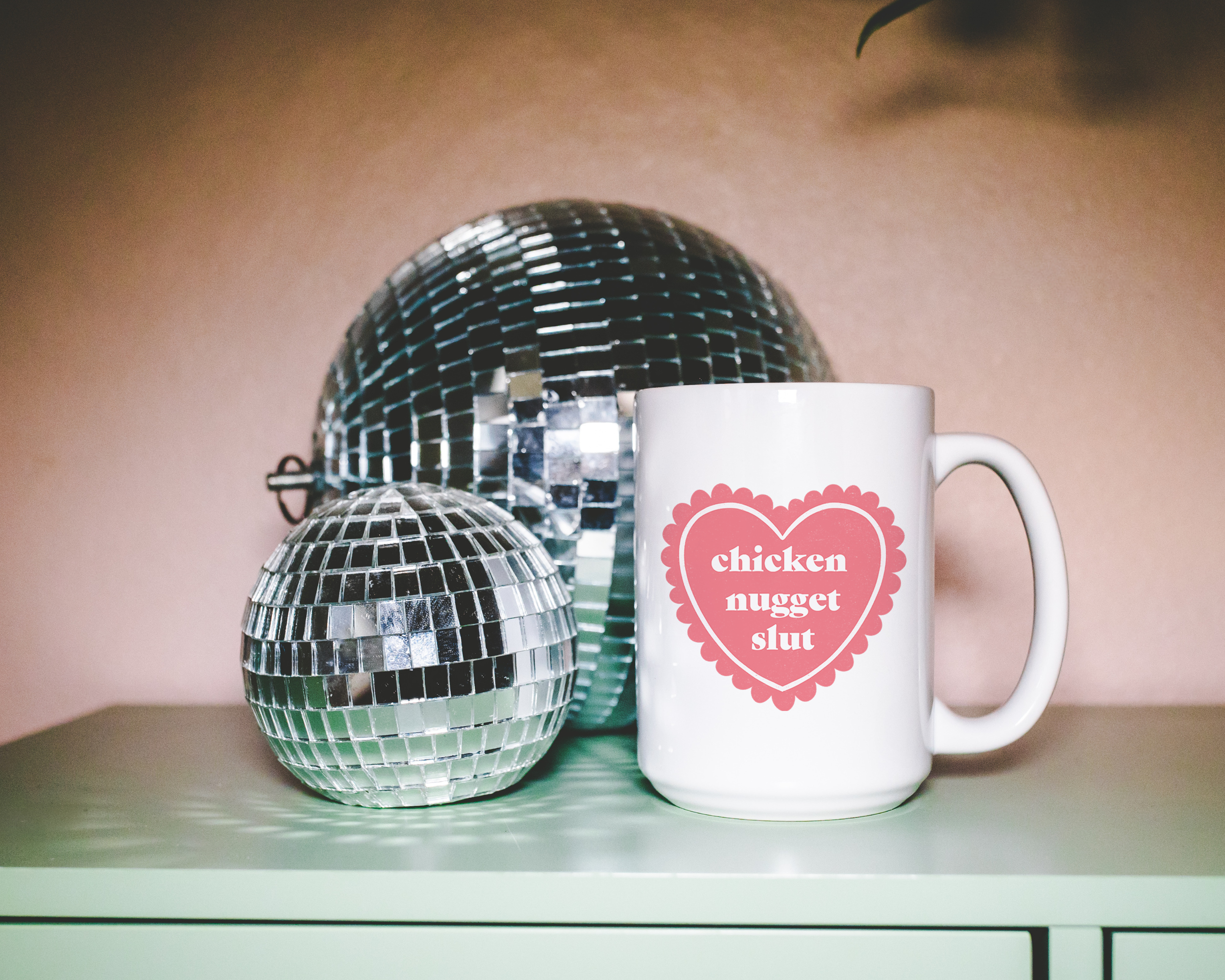 Sassy dopamine decor White coffee mug that says "chicken nugget slut" in a retro vintage style frilly heart that's pink with a retro font.. Available in 11oz and 15oz