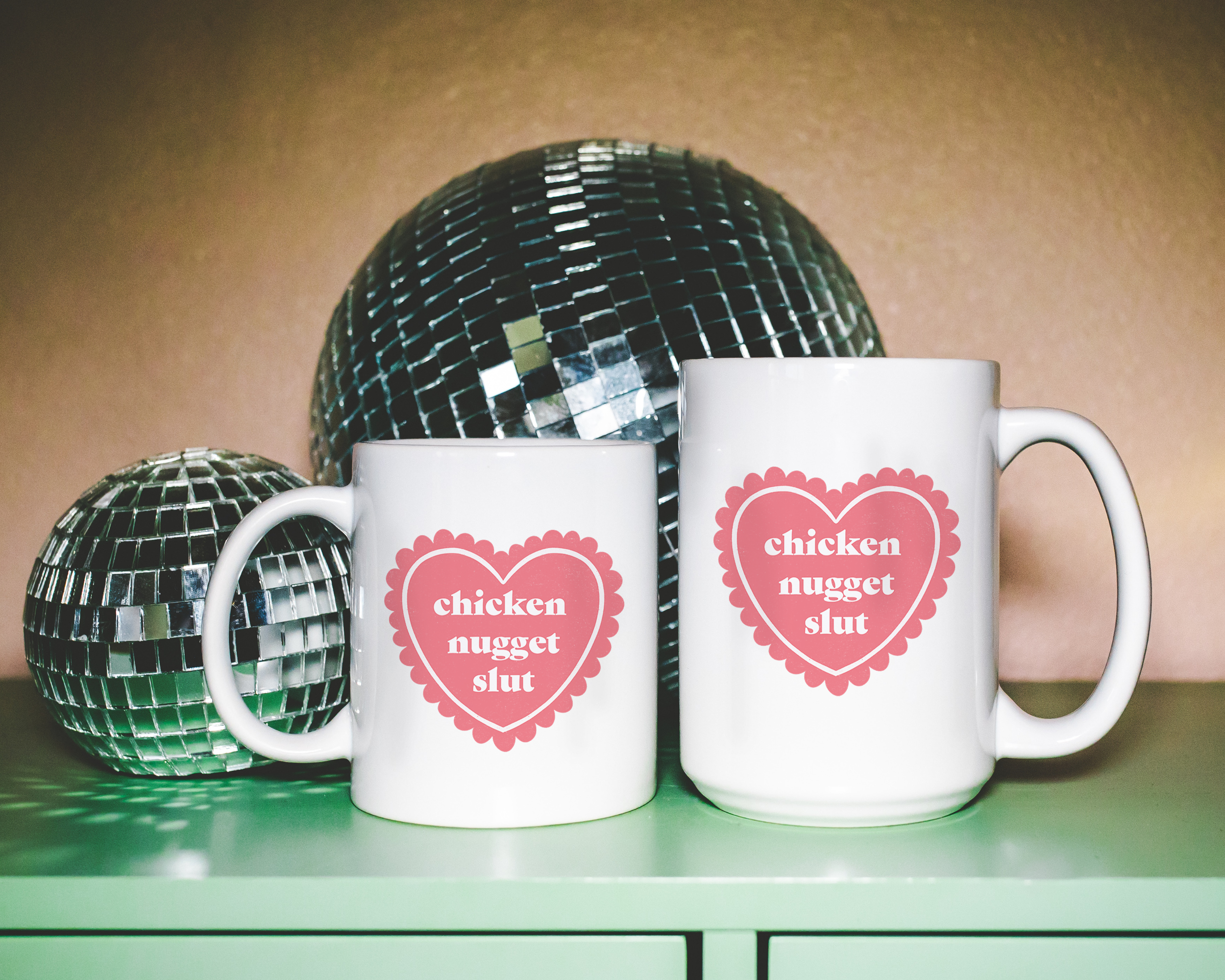 Sassy dopamine decor White coffee mug that says "chicken nugget slut" in a retro vintage style frilly heart that's pink with a retro font.. Available in 11oz and 15oz