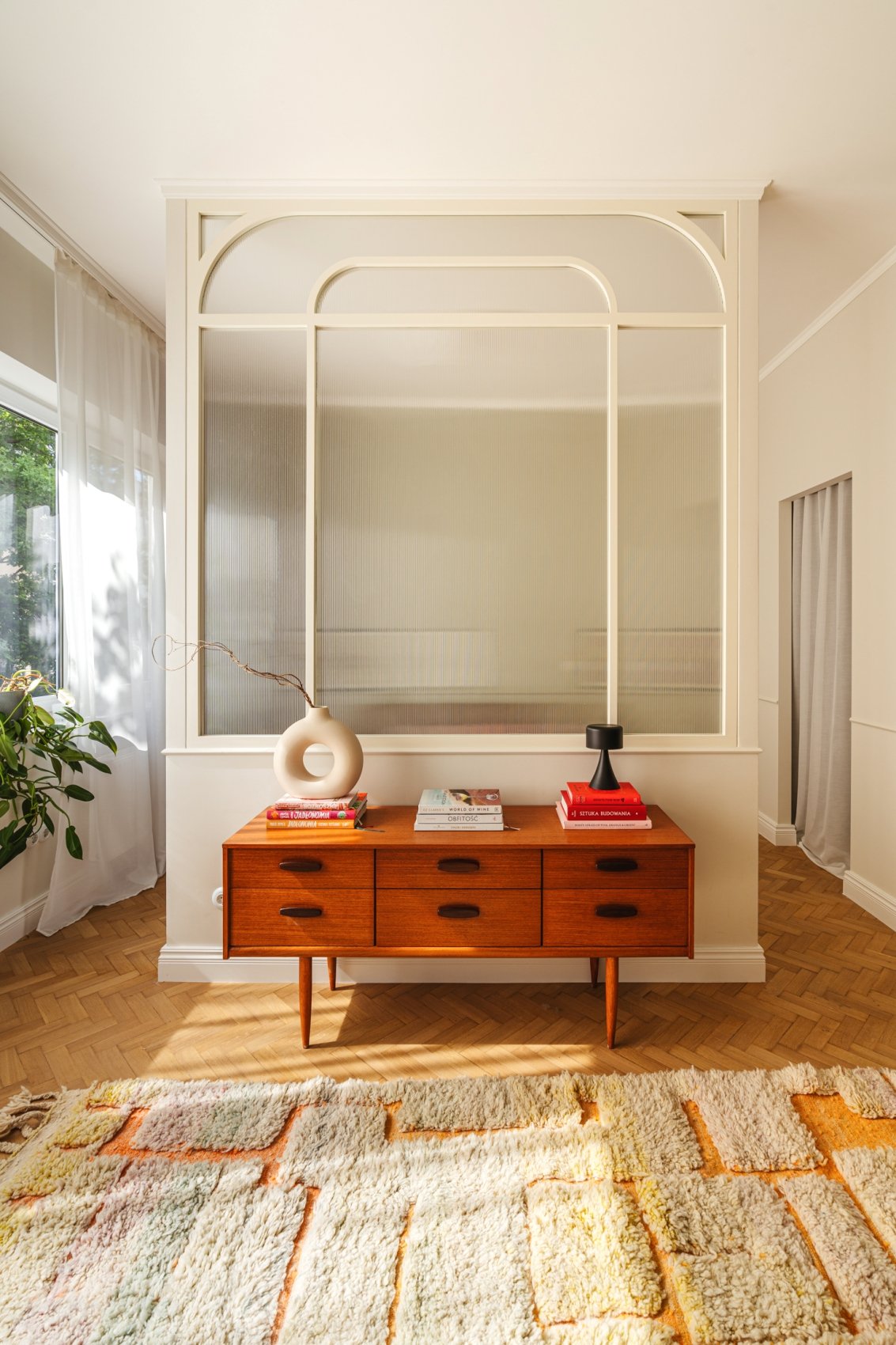 Une pièce avec un mur en verre, une console en bois avec des livres et des décorations.