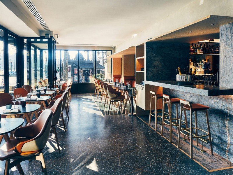 Intérieur d'un restaurant ou bar moderne avec des tables et des chaises en bois, et un comptoir de bar avec des bouteilles d'alcool