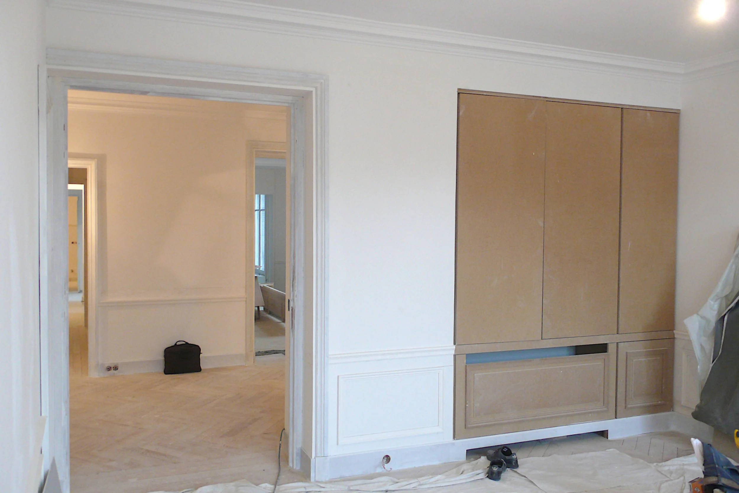 Intérieur d'une pièce en rénovation, avec un placard en bois encastré et une porte ouverte menant à une autre pièce
