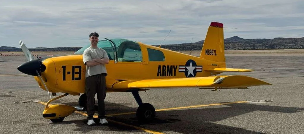 Person standing next to yellow aircraft with military markings on a runway.