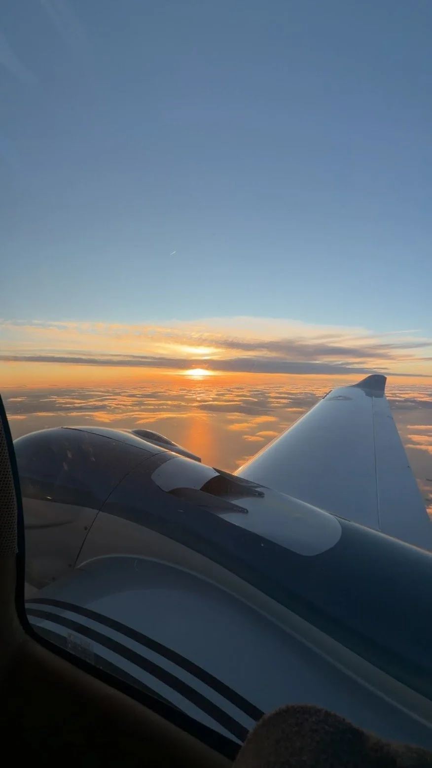 View of an airplane wing during sunset above the clouds.