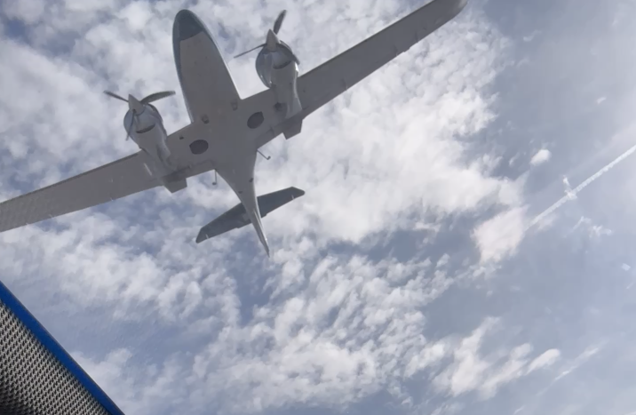 A white twin-engine propeller airplane flying in the sky with clouds.