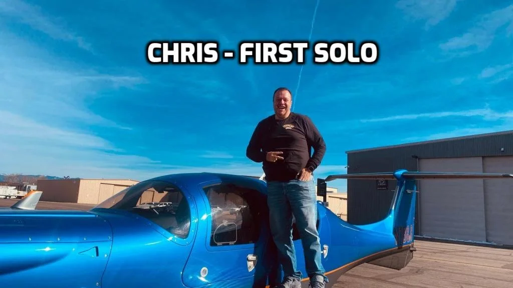 A man standing next to a blue race car on a rooftop under a blue sky with some clouds, with text overlay that reads 'Chris - First Solo'.