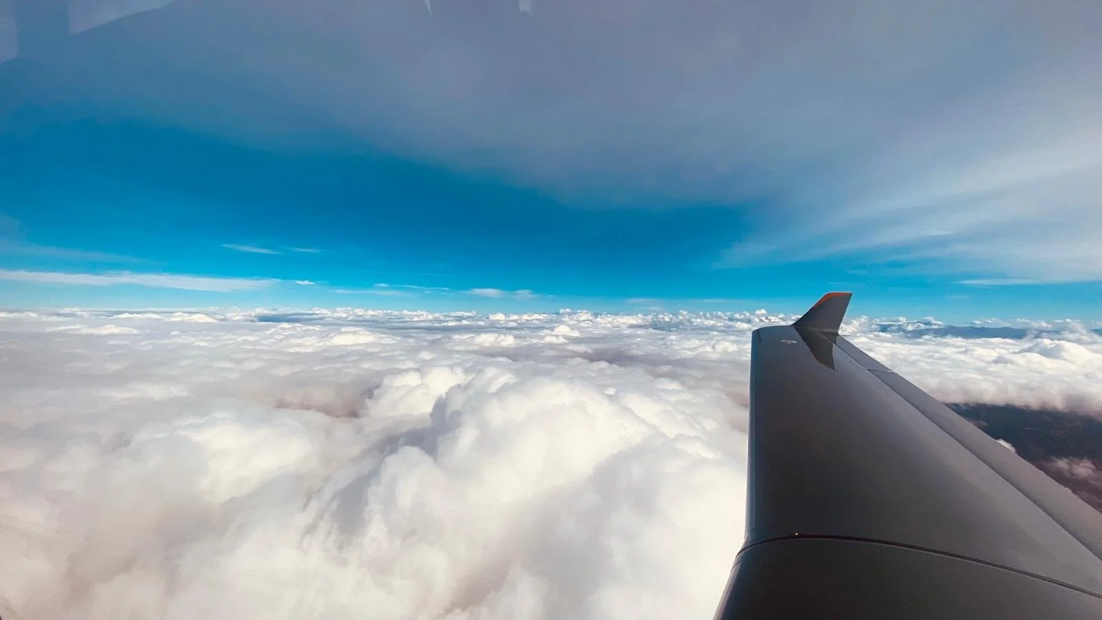 View from an airplane window showing the airplane wing and a sky filled with clouds.