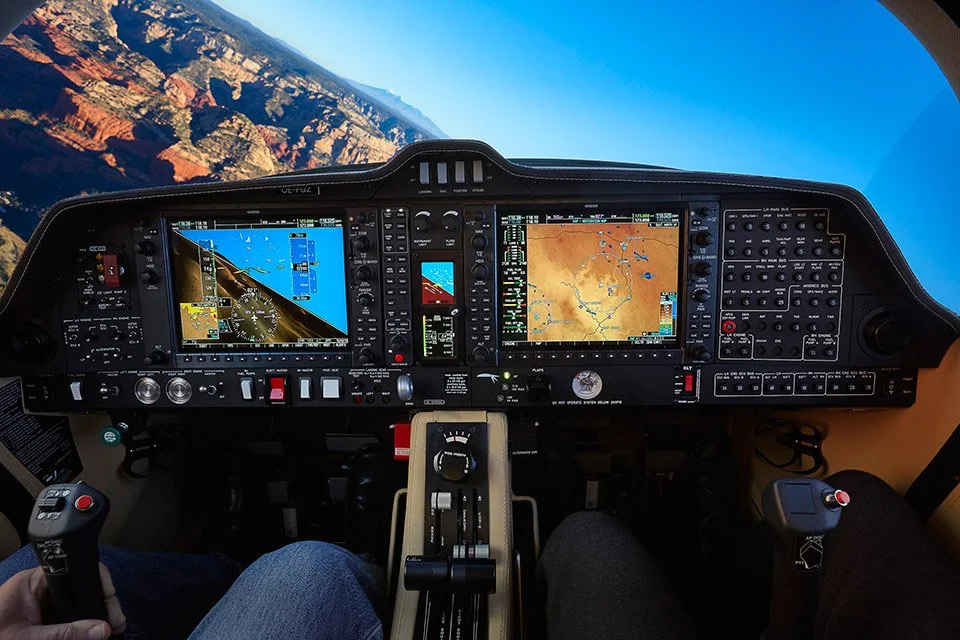 View from the cockpit of a plane flying over a canyon with rugged terrain, clear weather, and a blue sky.