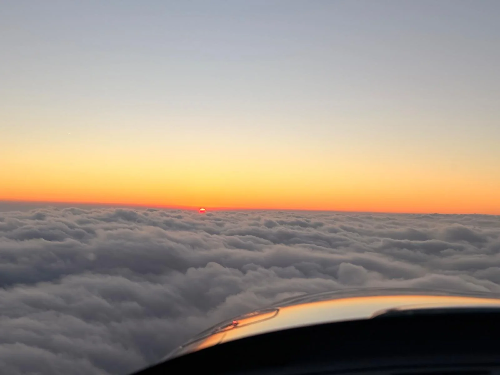 Sunset over clouds with a view from an airplane window, showing part of the airplane's wing.