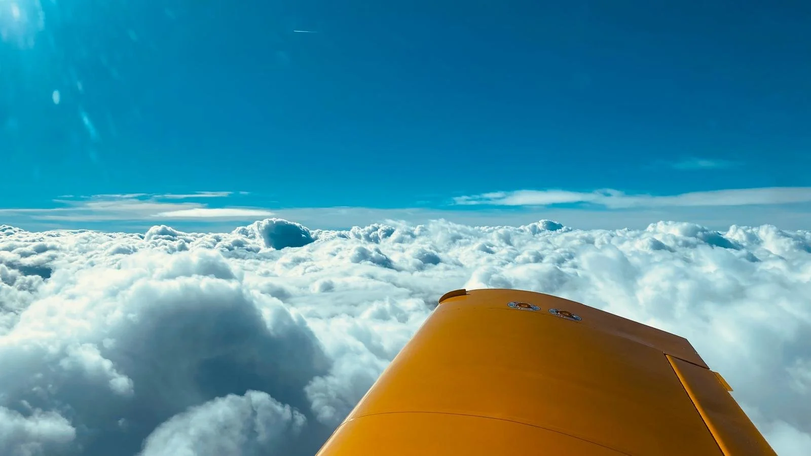 View from an aircraft window showing the yellow wing against a backdrop of clouds and blue sky.