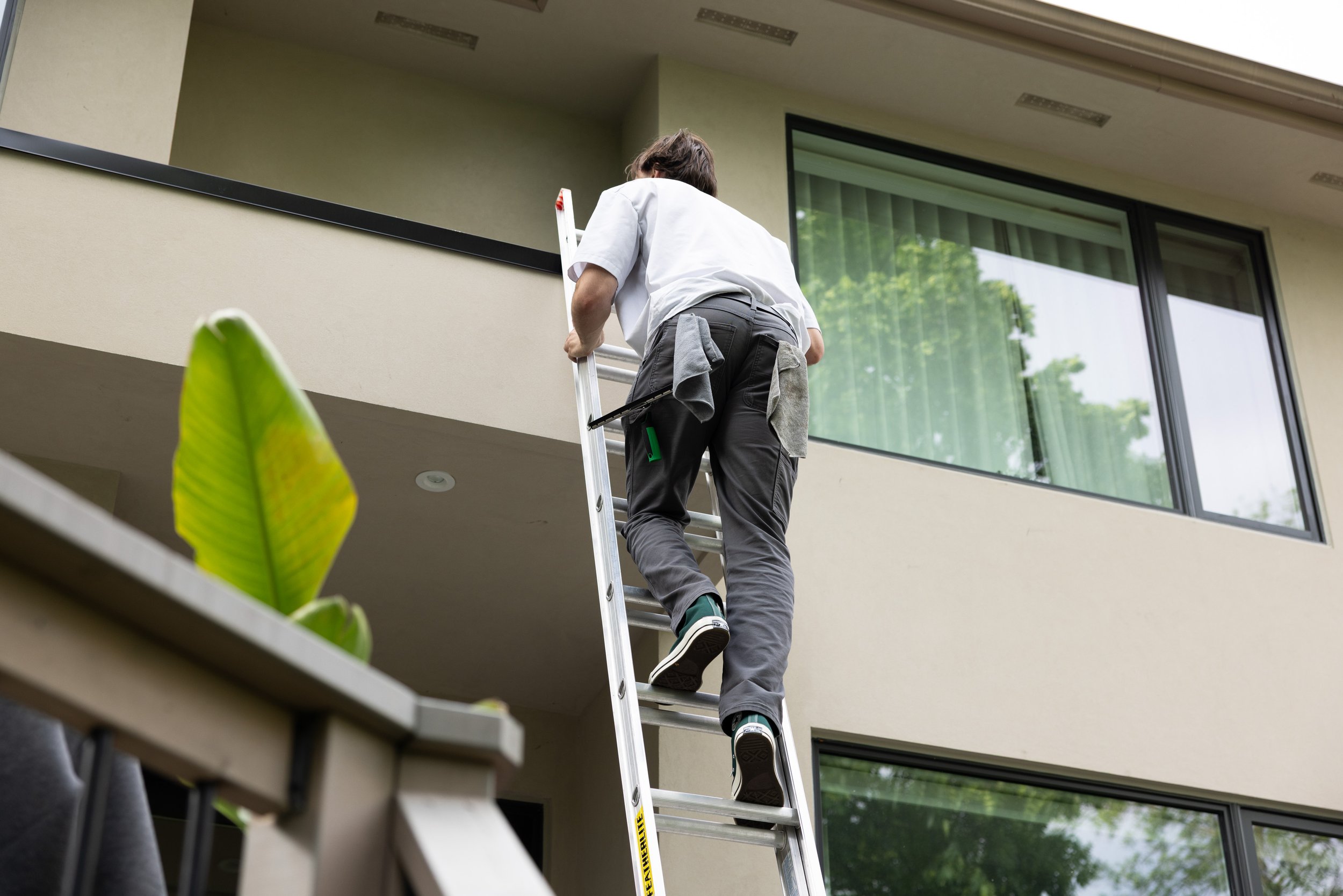 Worker climbing a ladder outside a modern apartment building with large windows.