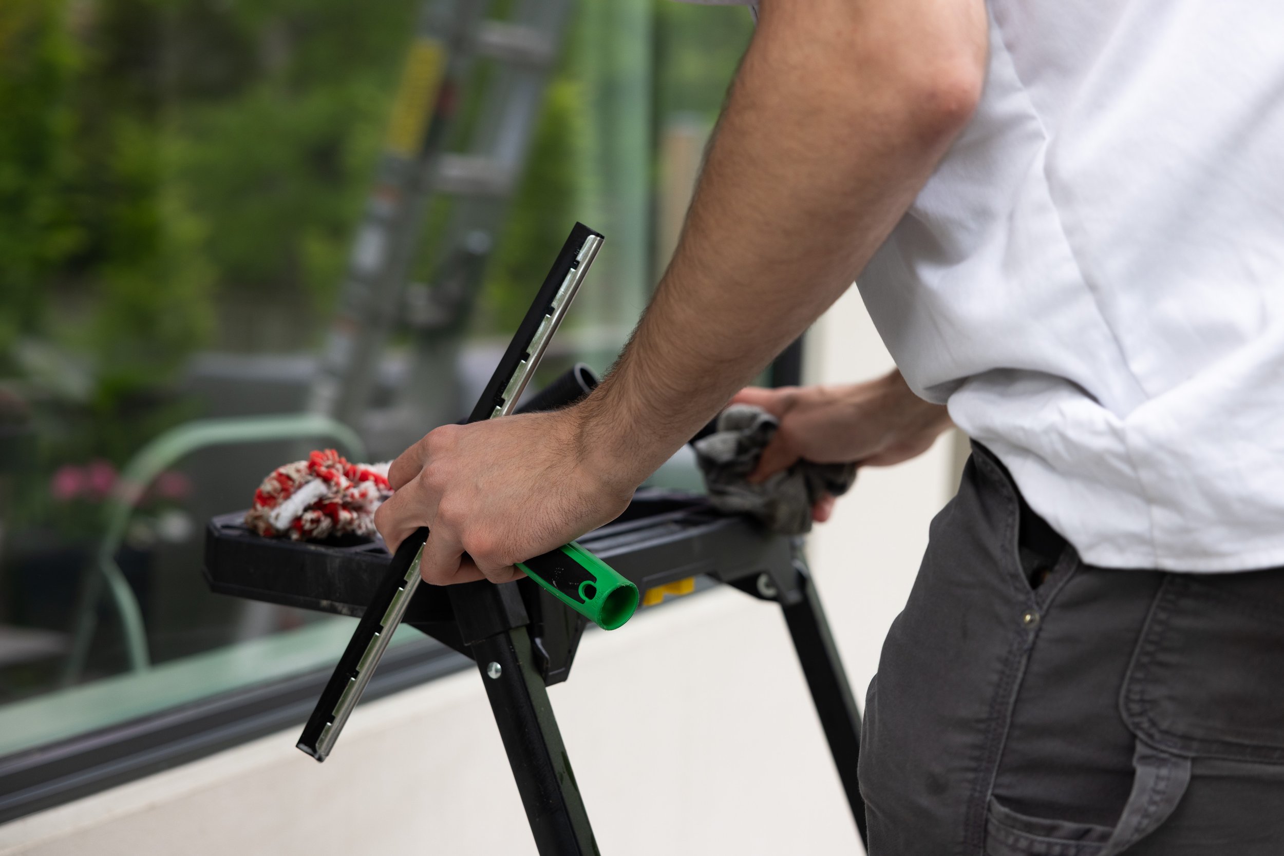 Person cleaning window with a cloth and squeegee on a balcony or patio.