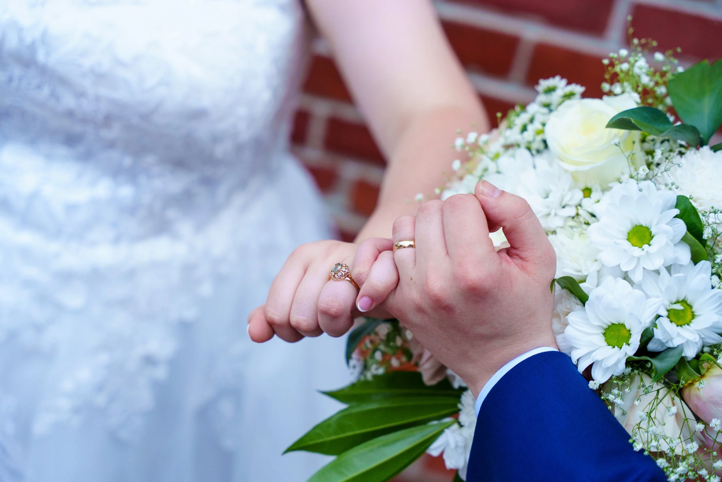 Close-up of a bride and groom holding hands during a wedding, with a bouquet of white flowers and greenery.