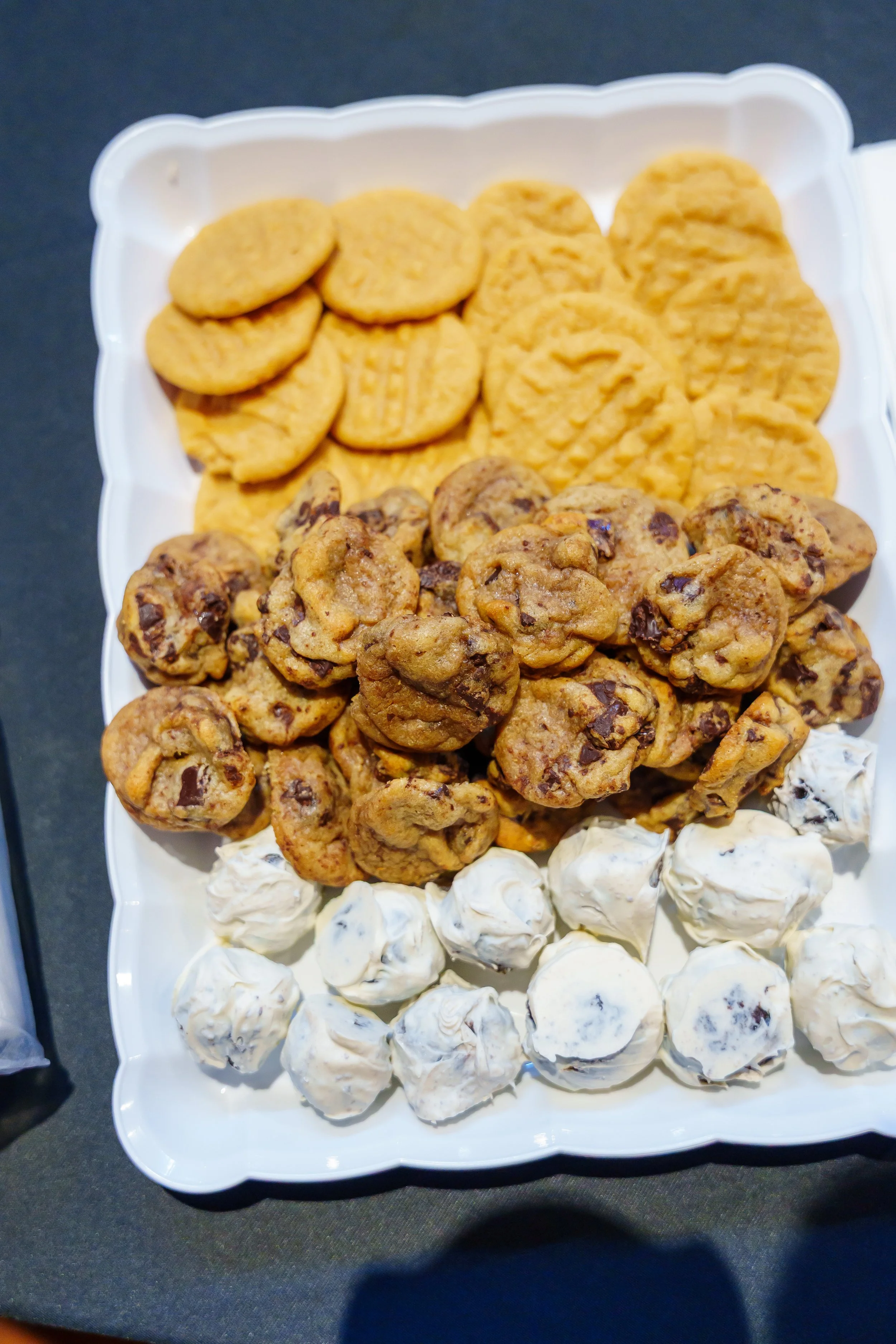 A white platter filled with assorted cookies including chocolate chip, oatmeal, peanut butter, and swirl cookies, arranged in sections.