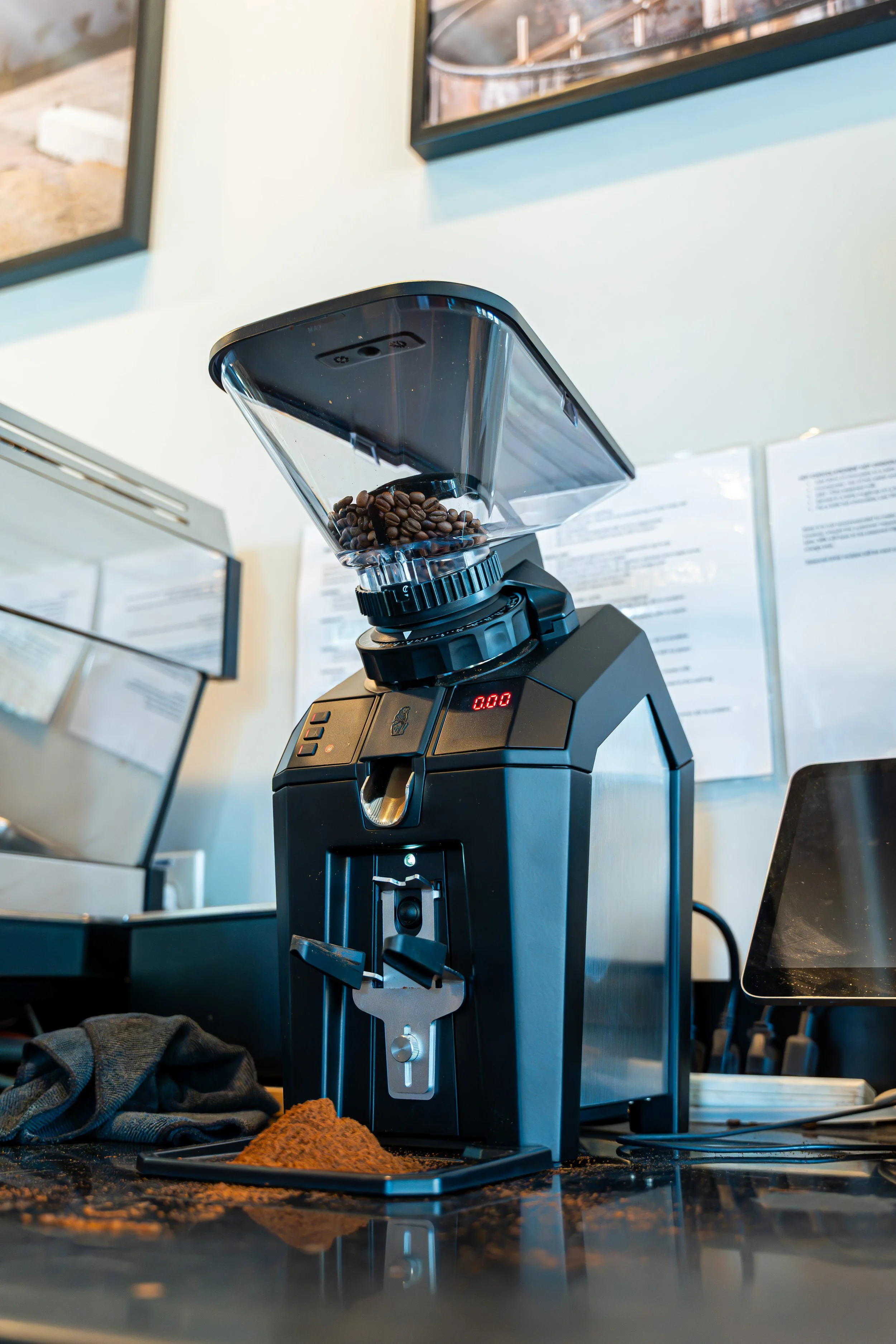 Close-up of a coffee grinder with coffee beans inside, on a counter in a cafe or kitchen.