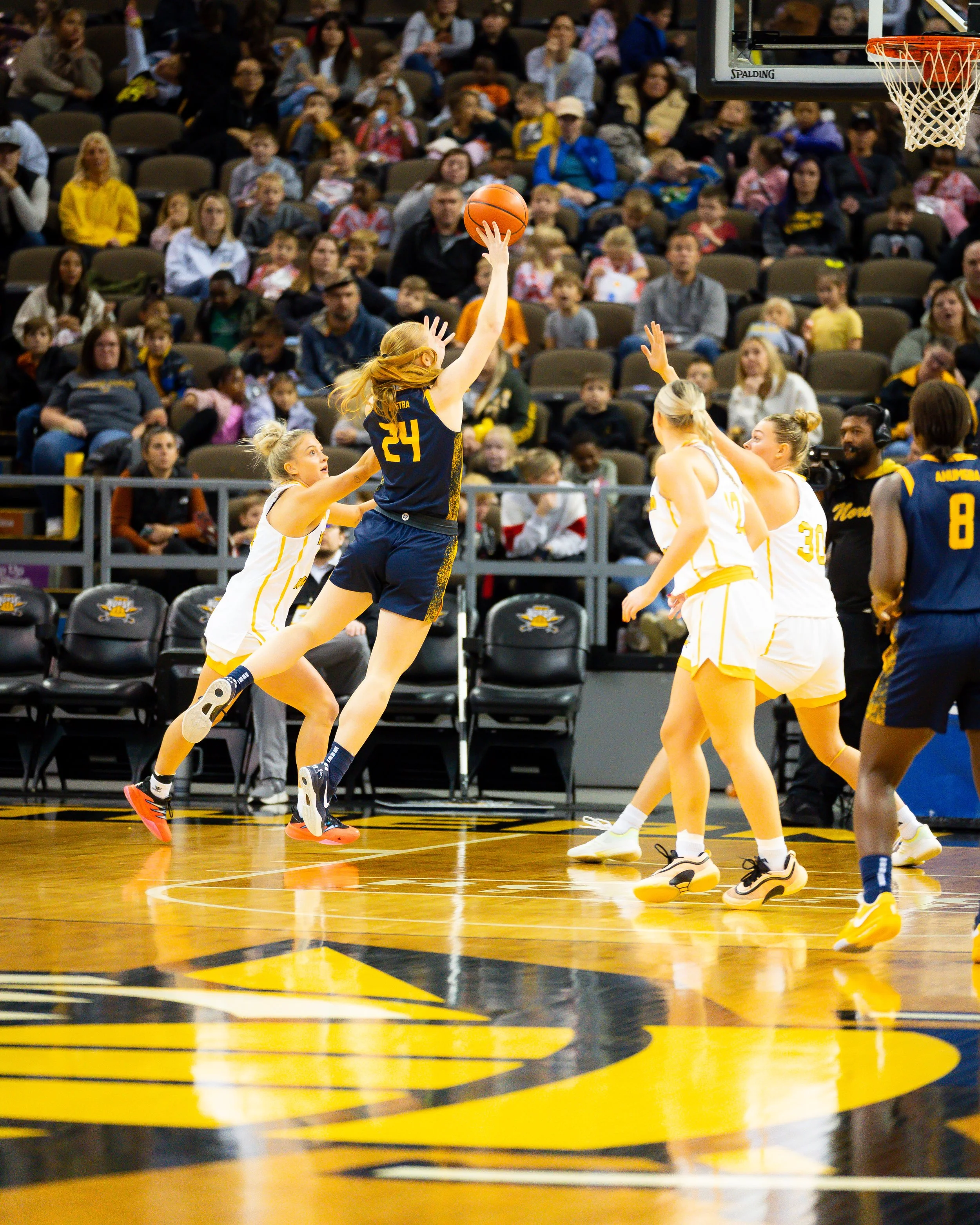 Women playing basketball on a court, with a crowd of spectators in the background.