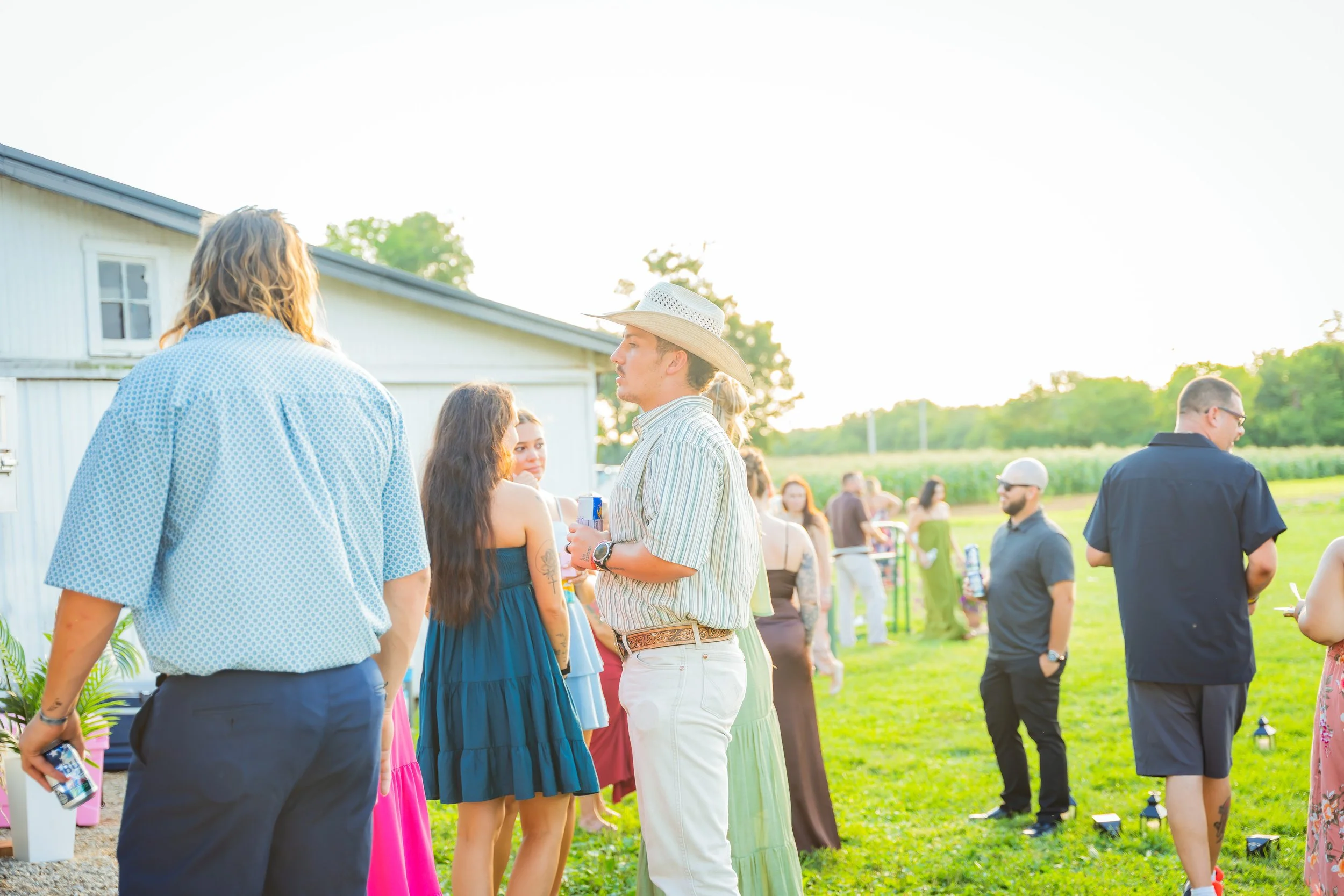 People gathering outdoors in a backyard, socializing, with a group of women in colorful dresses and men in casual attire, during late afternoon or early evening.