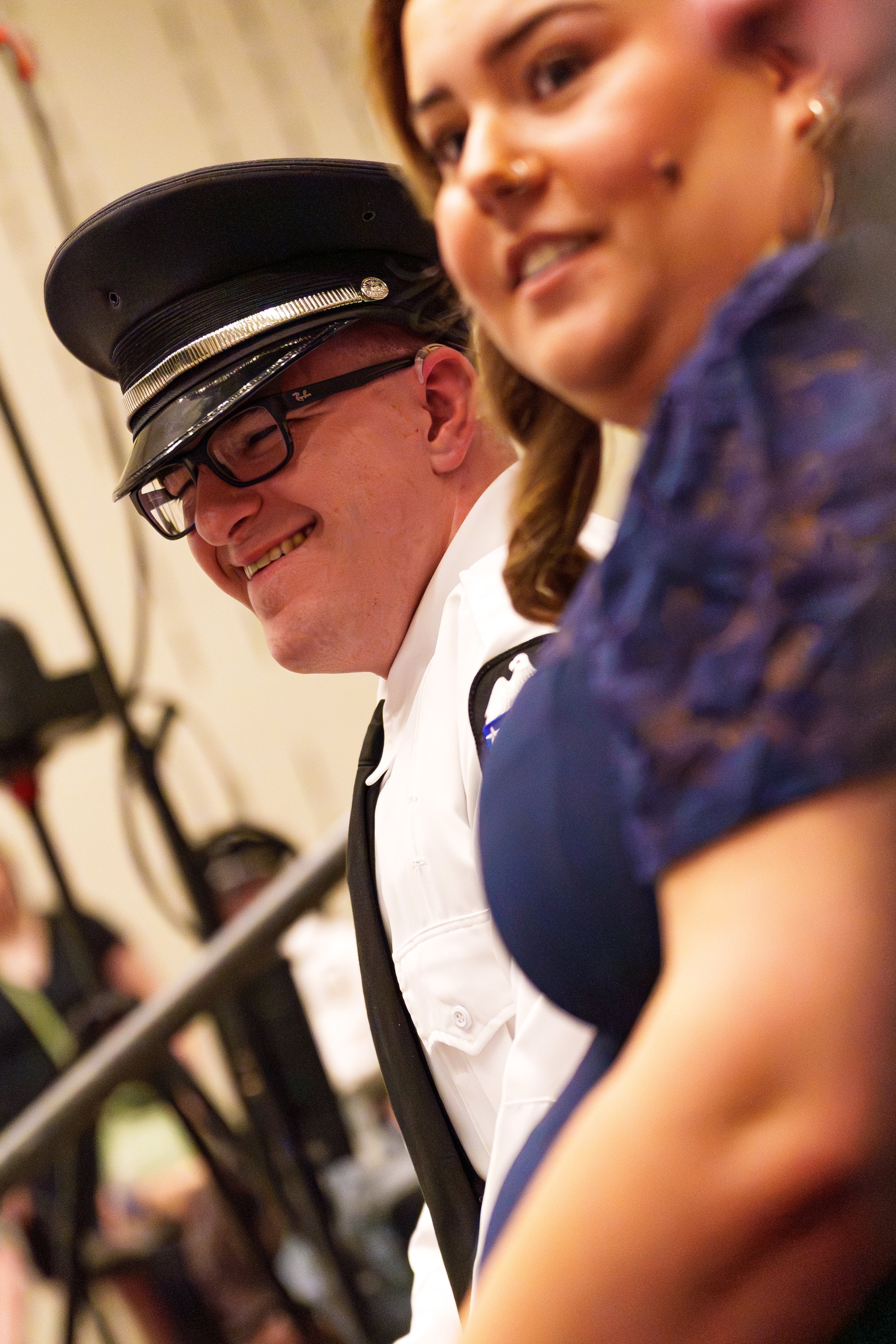 Close-up of three smiling children, one wearing glasses and a police officer's hat, at an indoor event.