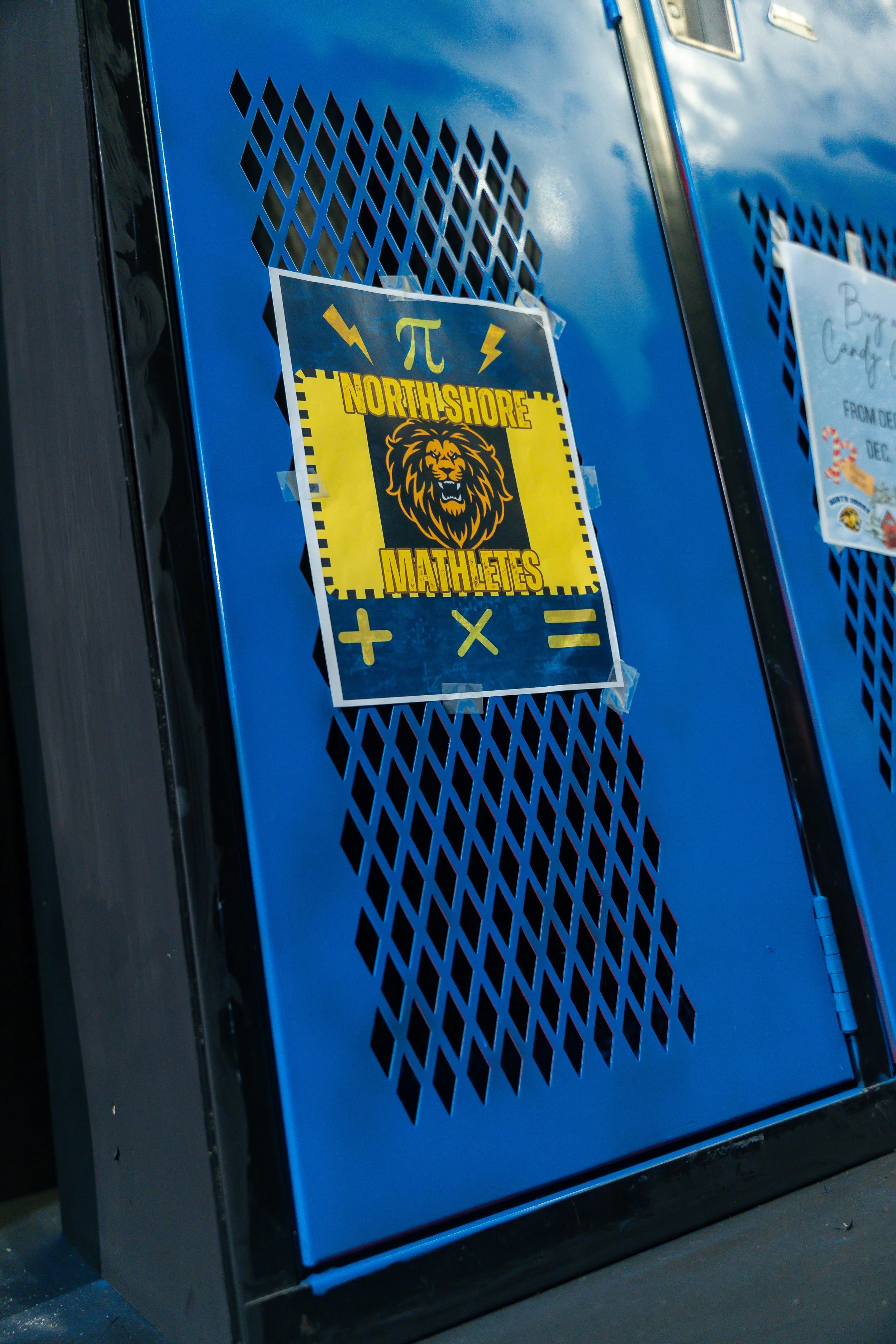 Blue locker with a sign that reads "North Shore Mathemletes," featuring a lion's face, mathematical symbols, and a background of a clear sky with clouds.