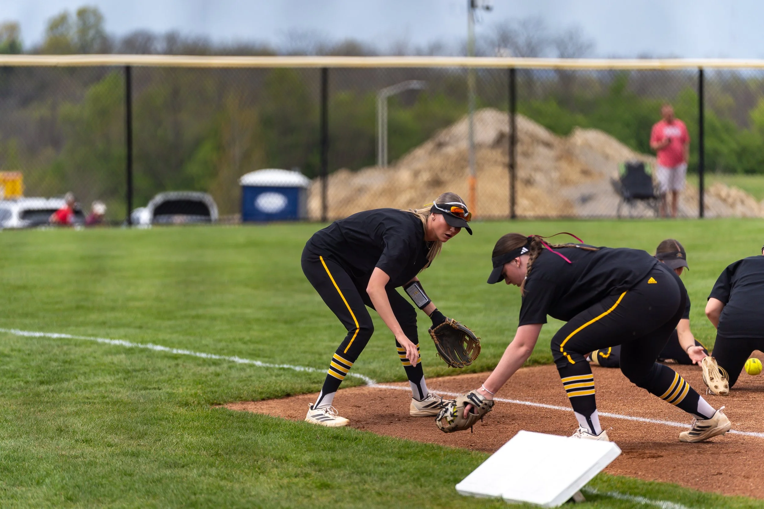 Girls in black and yellow uniforms practicing soft toss in softball field.