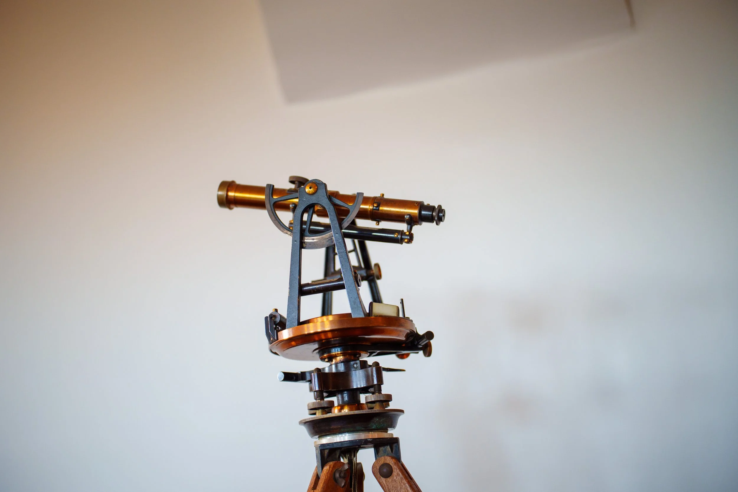 Close-up of an antique brass and metal telescope mounted on a wooden tripod against a plain light-colored background.