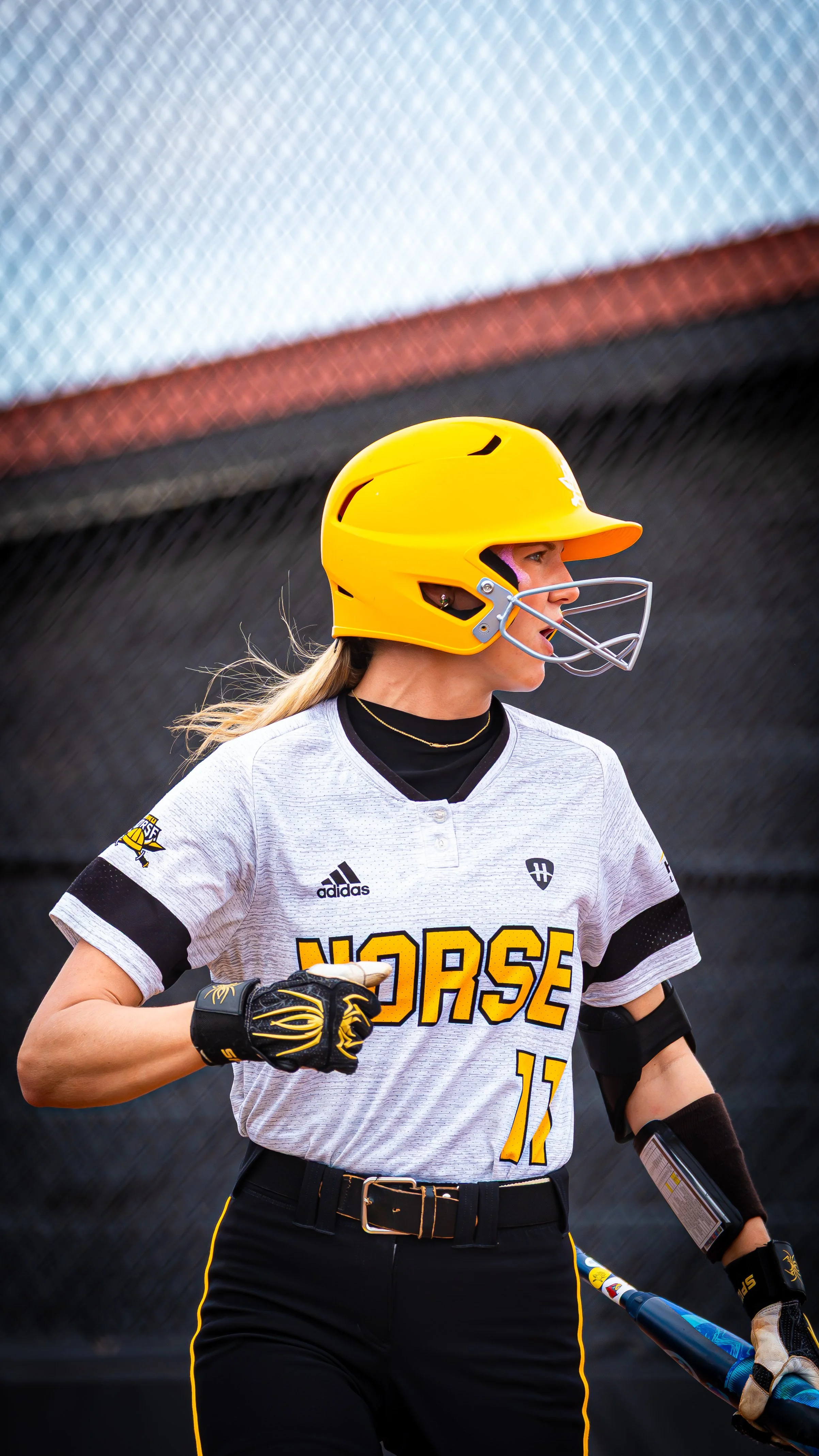 A female softball player wearing a yellow helmet and a gray uniform with black and yellow accents, holding a baseball bat during a game.