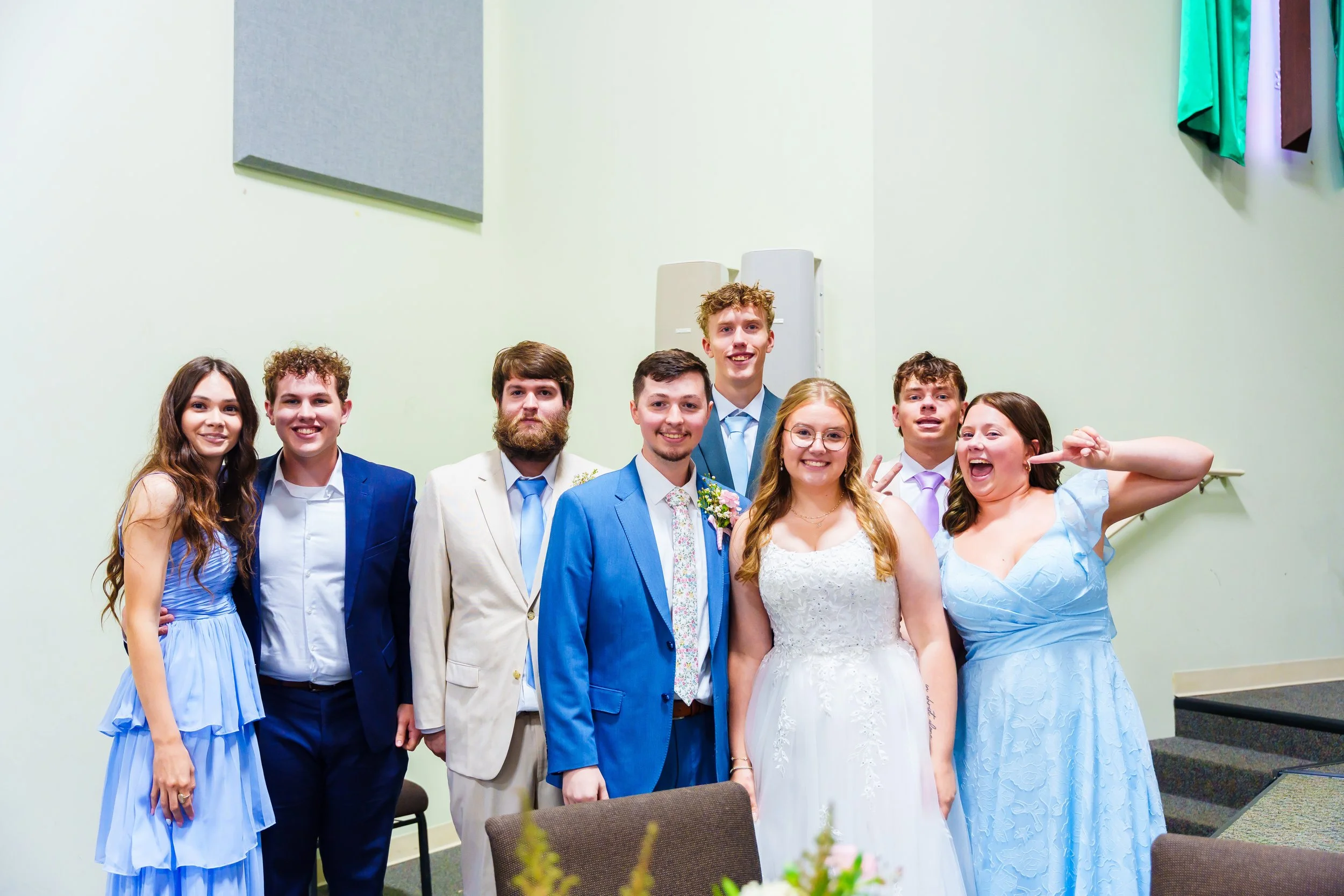 Group of young people dressed in formal attire at a celebration, standing indoors against a green wall.