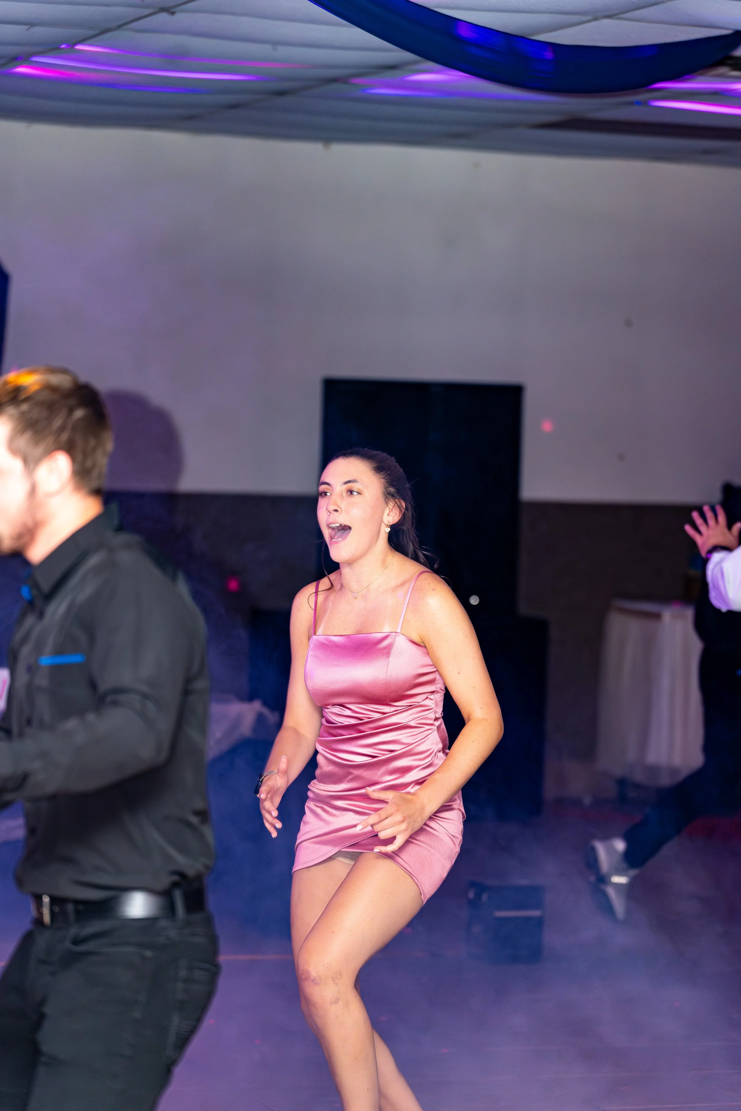 Woman in pink satin dress dancing at a party or event with colorful lighting.