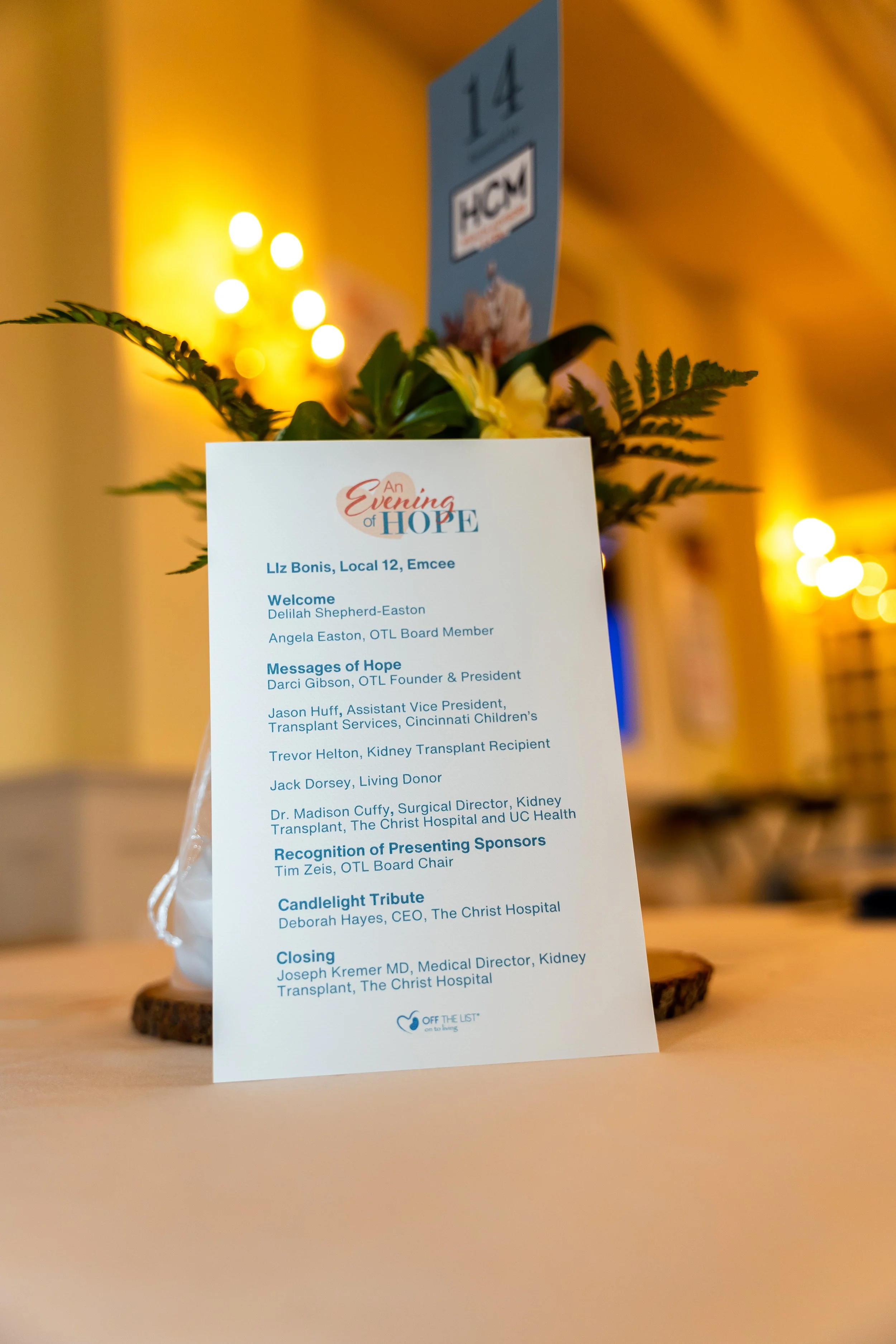 A printed program or agenda for an event titled "An Evening of Hope", standing on a wooden surface with background lighting. The program lists speakers and acknowledgments including Liz Bonis, Delilah Shepherd-Easton, Angela Easton, Darci Gibson, Jas