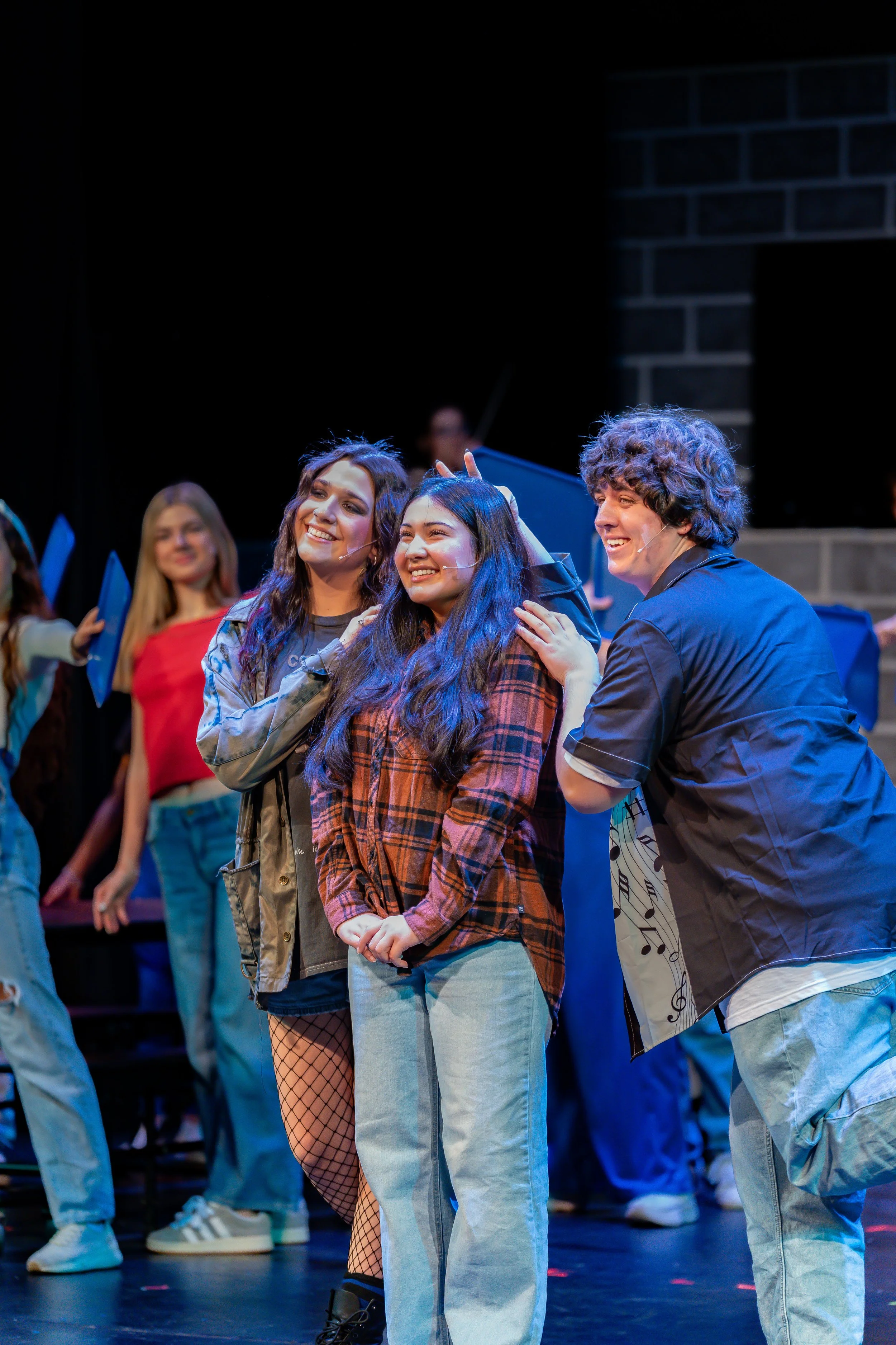Group of young performers on stage during a rehearsal or performance, smiling and interacting with each other.