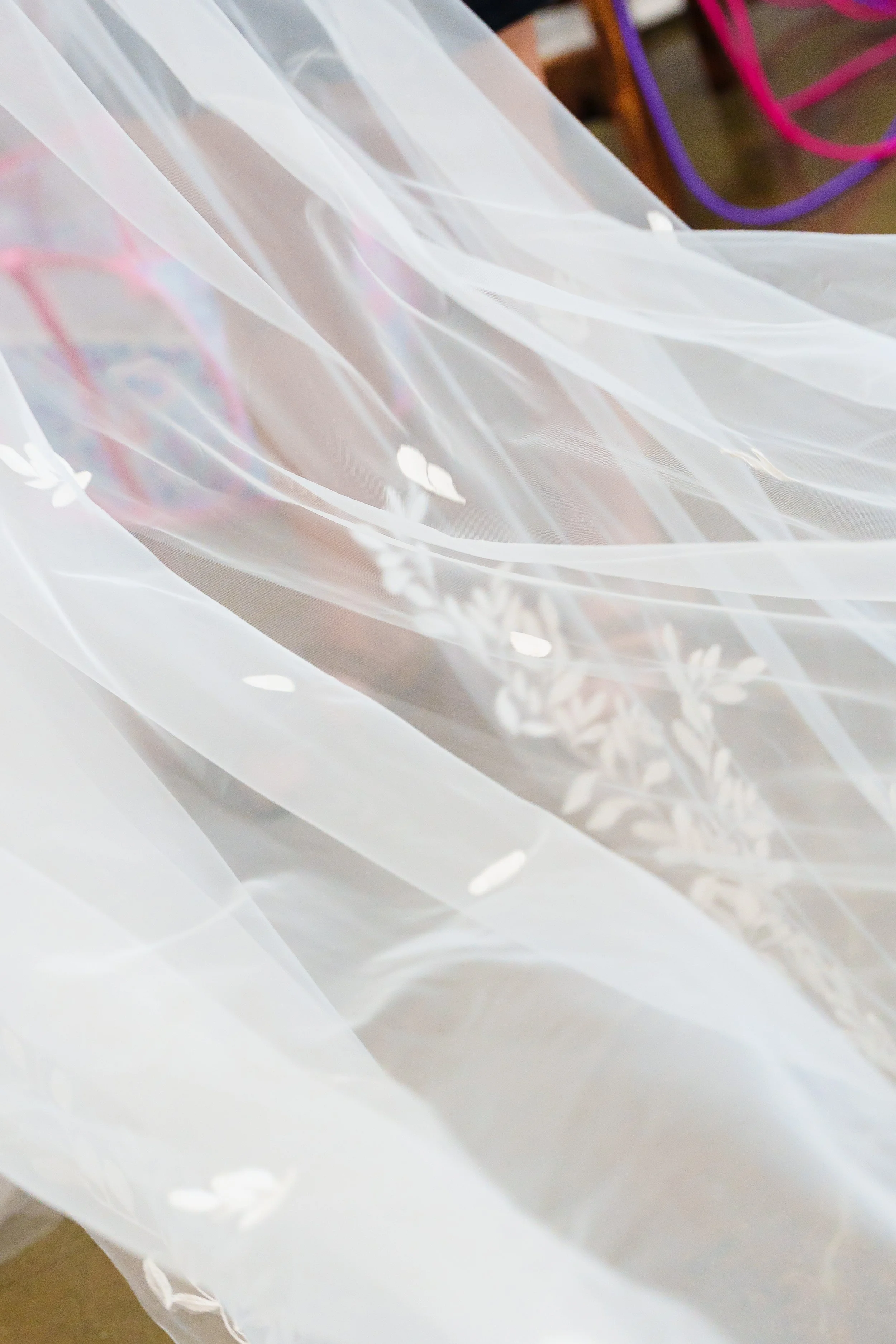 Close-up of a white, translucent decorative fabric with floral patterns, draped and illuminated by light.