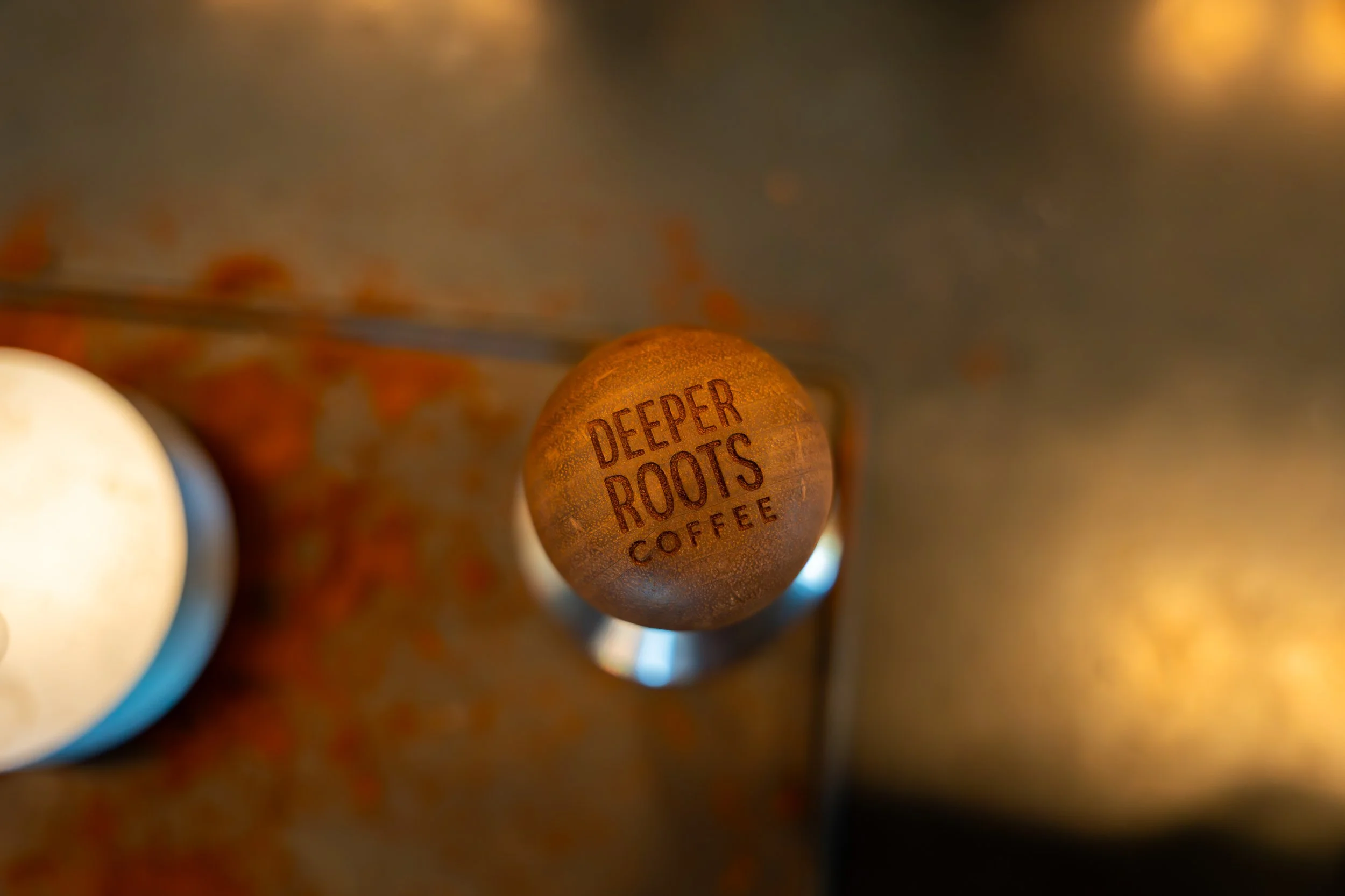Close-up of a round coffee capsule with the text 'Deeper Roots Coffee' printed on it, surrounded by blurred coffee beans.