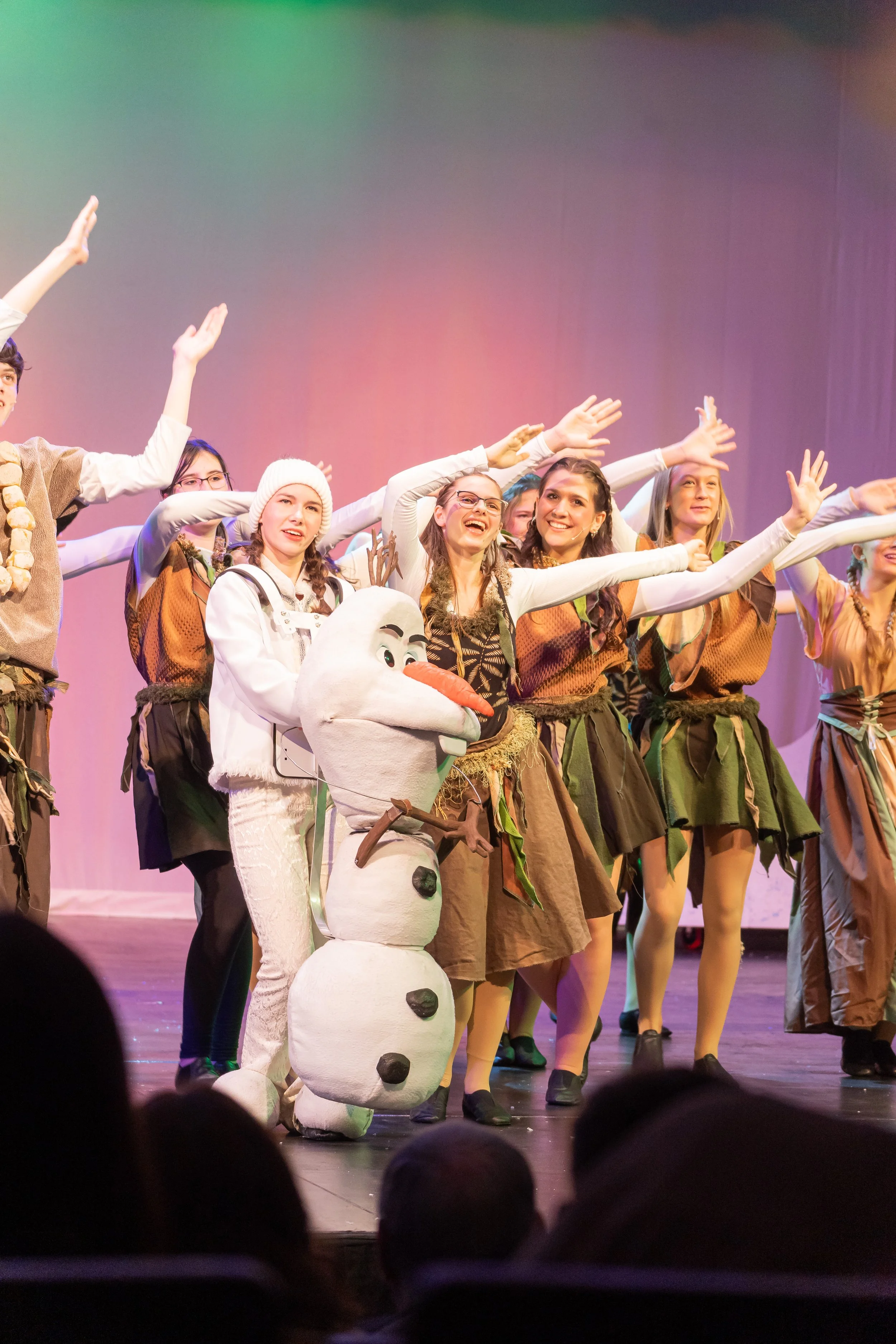 Aspect of a stage performance with actors dressed as characters from Frozen, including Olaf the snowman, and dancers in Viking-inspired costumes, with an audience in the foreground.